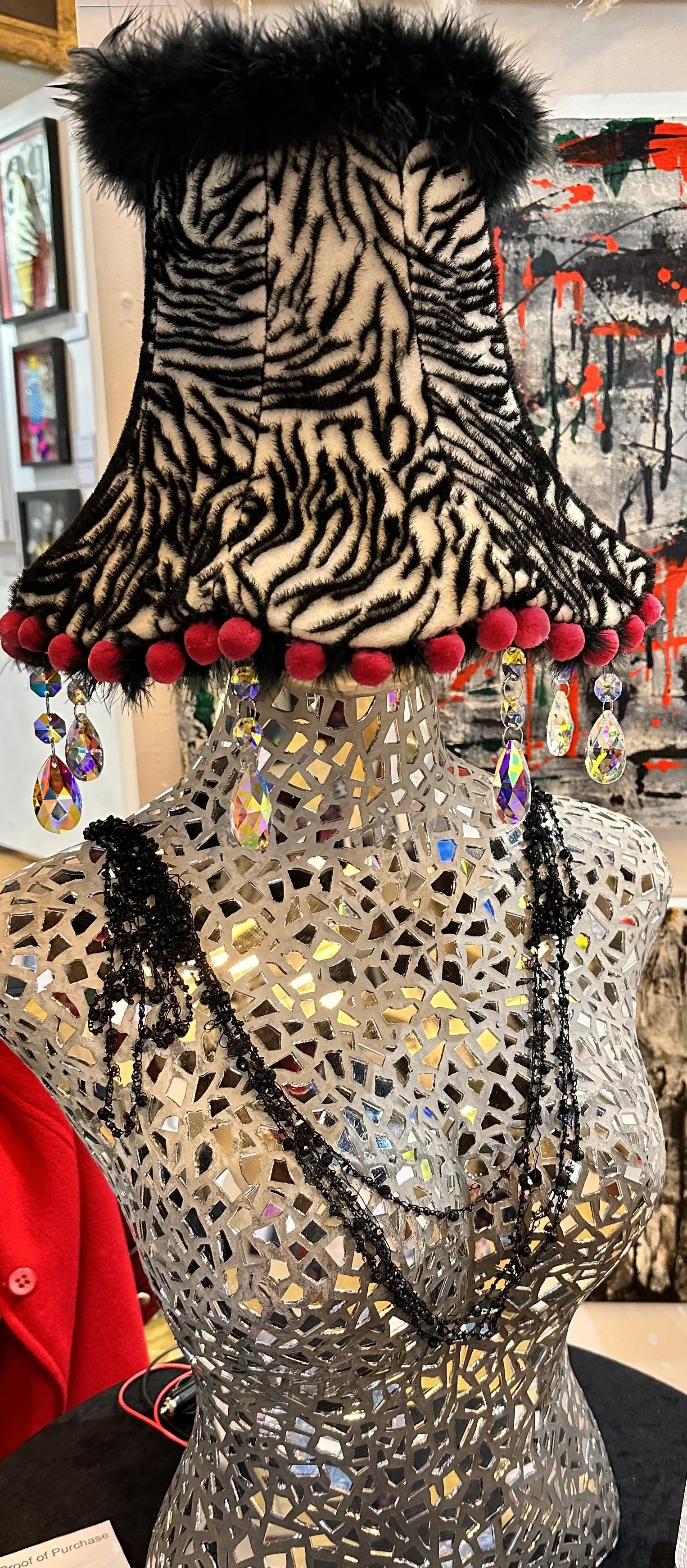 The sculpture Boudicca Zebra Lamp on display at Art Fair East, showcasing the mirror reflections in the glass and the broken necklace along with glimpses of pink pom poms and black marabou feathers and a/b crystal droplets
