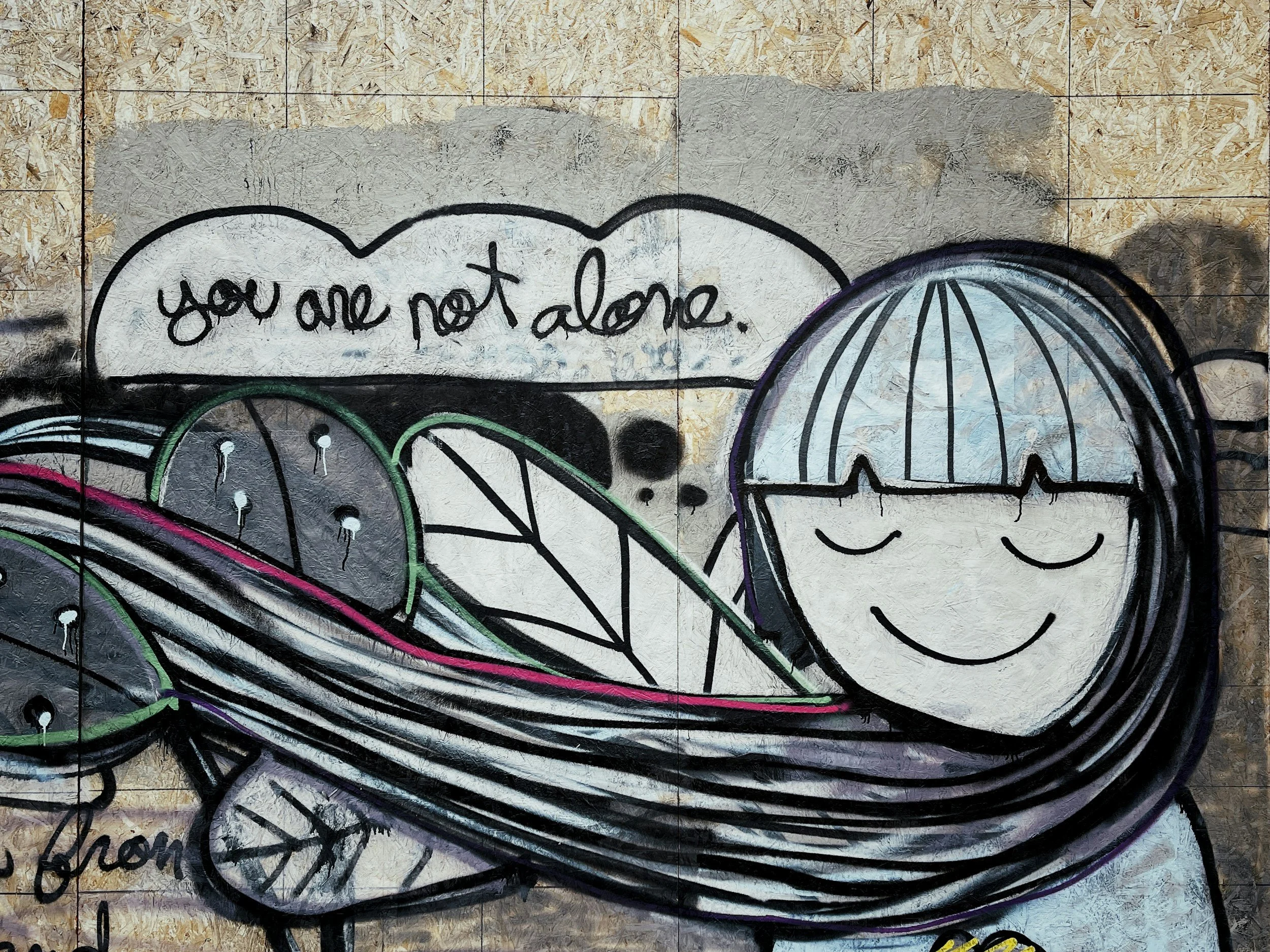 Street art graffiti of a smiling girl with closed eyes and short hair, holding a large bowl of fruits including watermelon slices, with a speech bubble that reads 'you are not alone.'