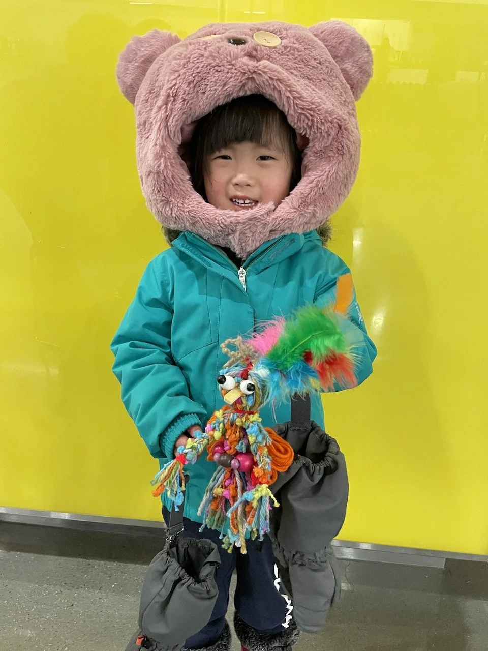 Child in pink furry hood holds a puppet she has made.