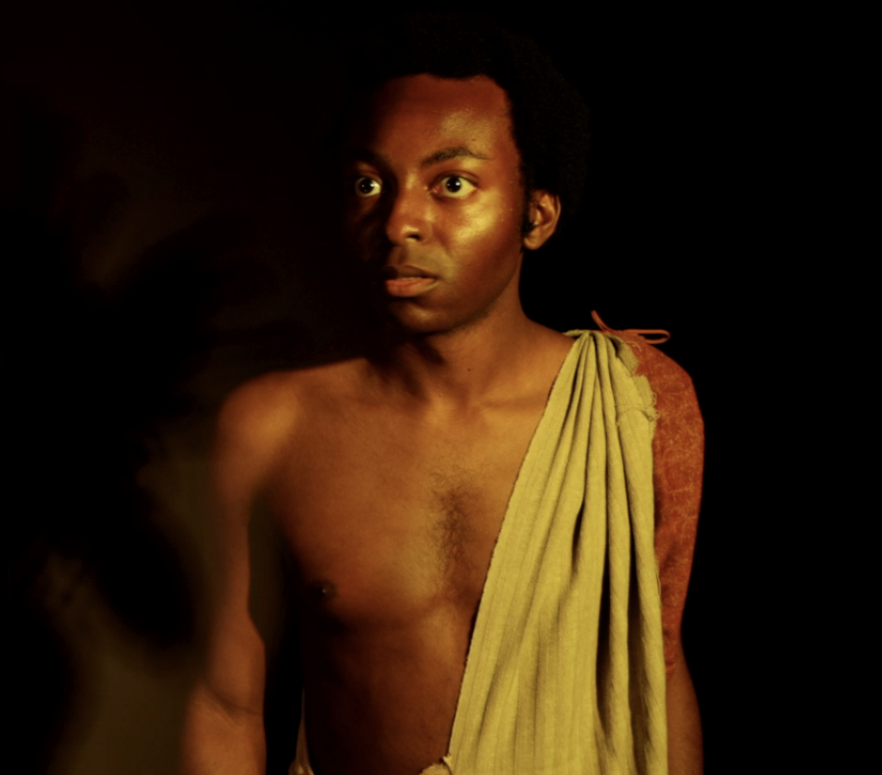 Black man in a yellow toga looks piercingly