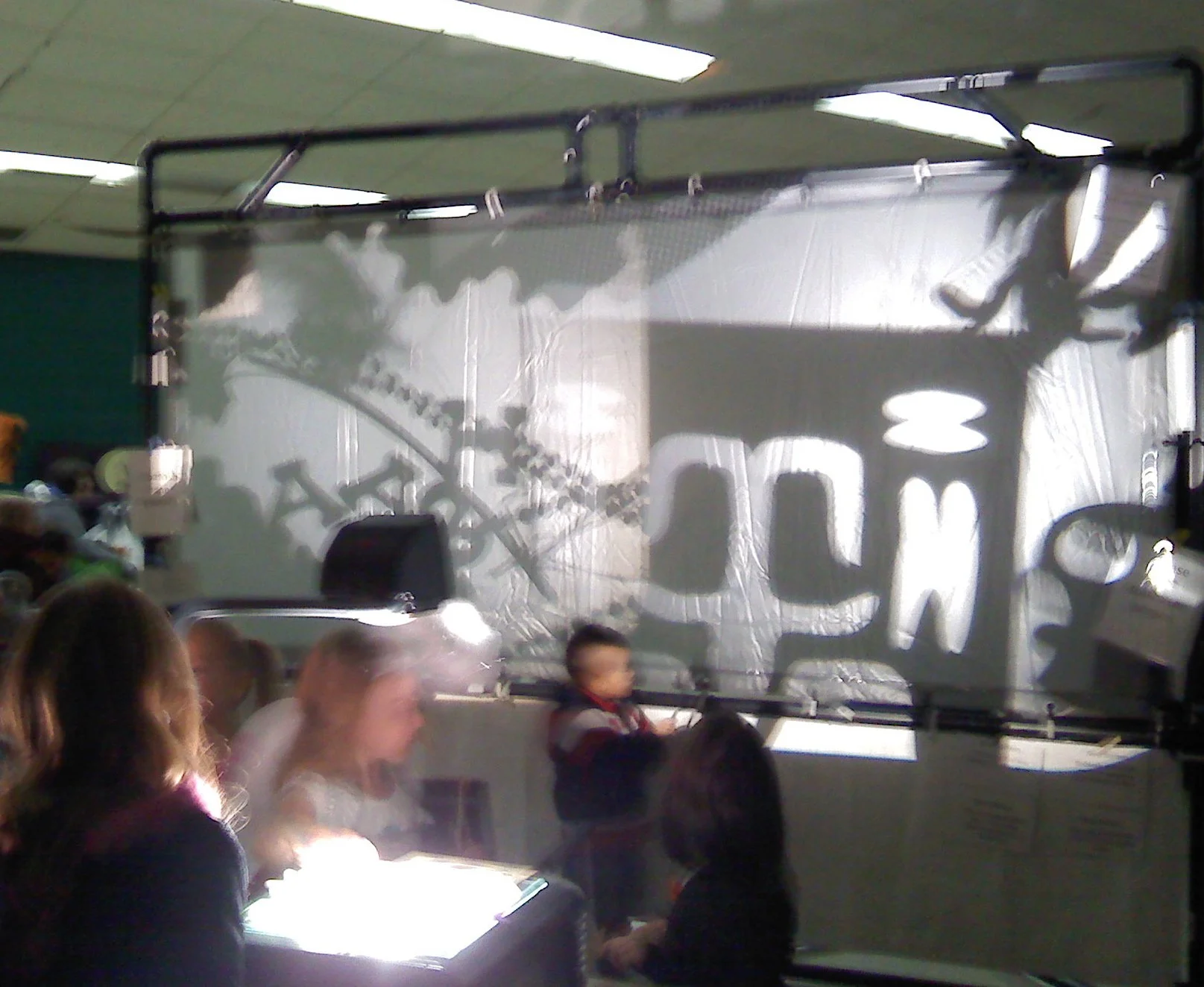 Slightly blurry image of children playing with shadow puppets, a screen and bright lights