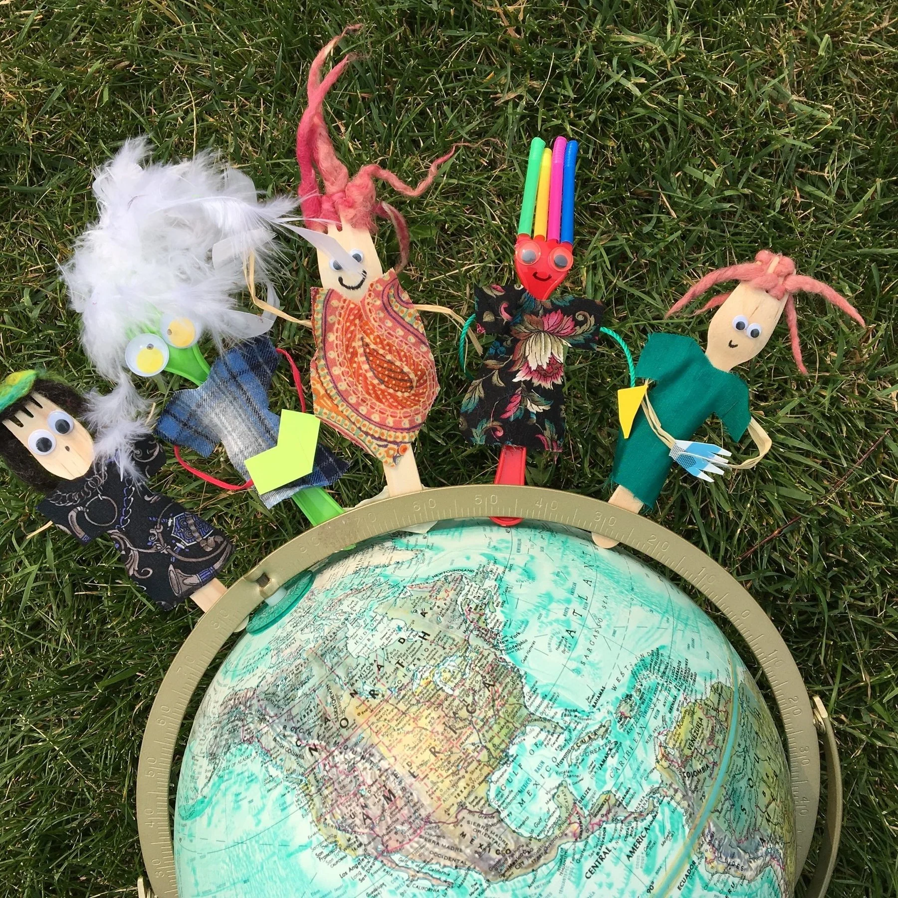 Forks, with colourful fabric and feathers decorations stand on a globe set onto some grass