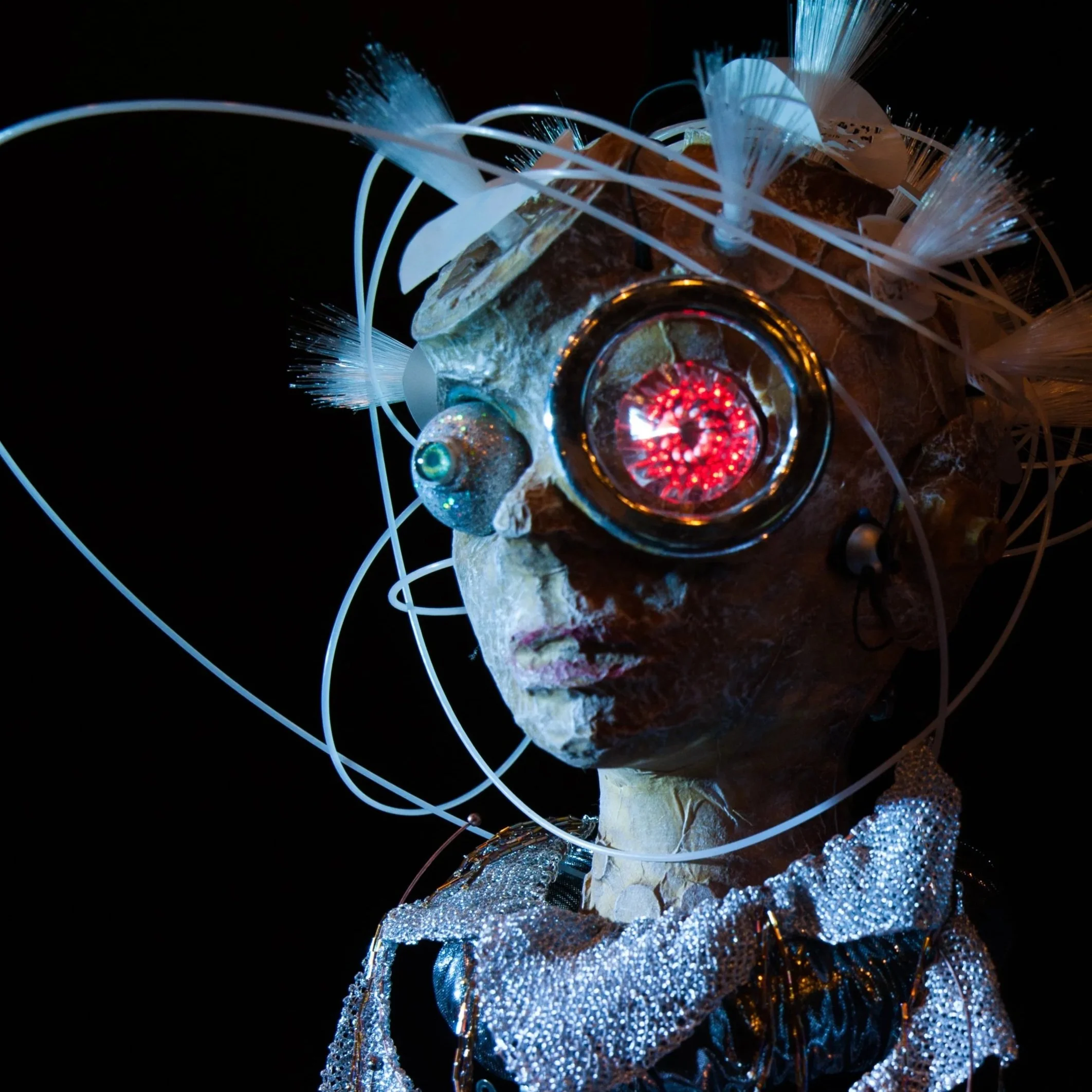 Cyborg puppet face with red eye and plastic cables