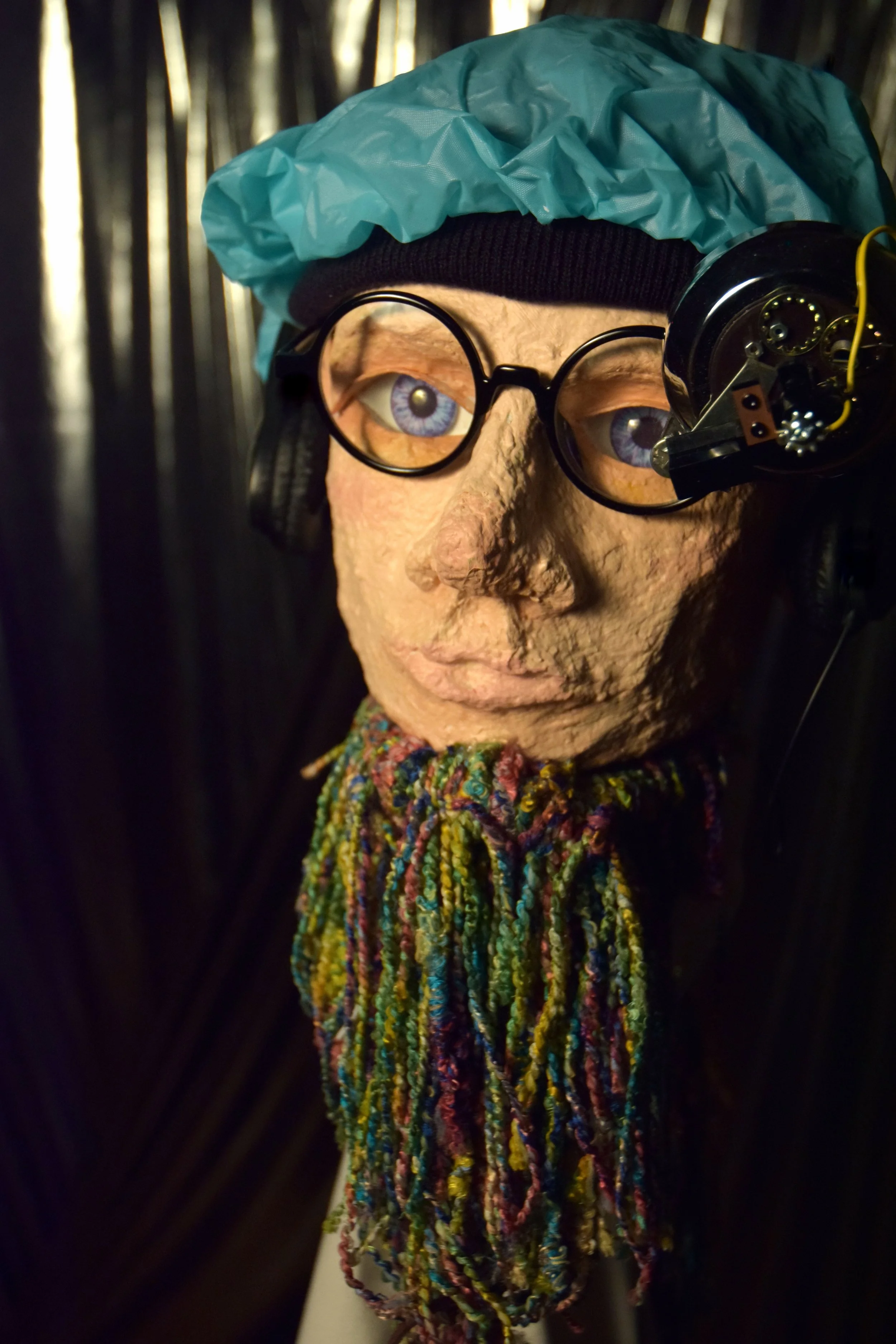 Human like puppet face with black glasses and a blue shower cap