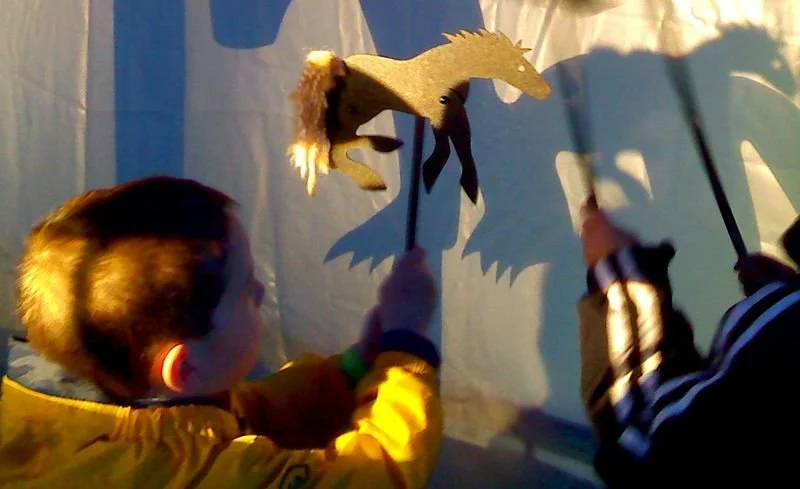 A child holding sticks and using a shadow puppet of a horse on a white backdrop.
