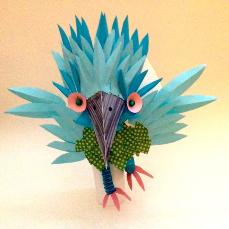 Paper craft of a colorful turkey with spiky blue and teal feathers, pink eyes, green dotted wings, and pink feet against a plain background.
