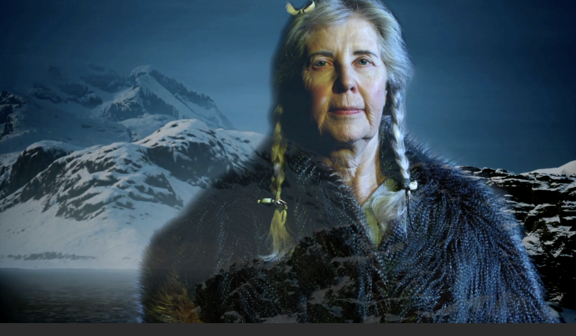 Women in furs and with braids stands in front of a mountain