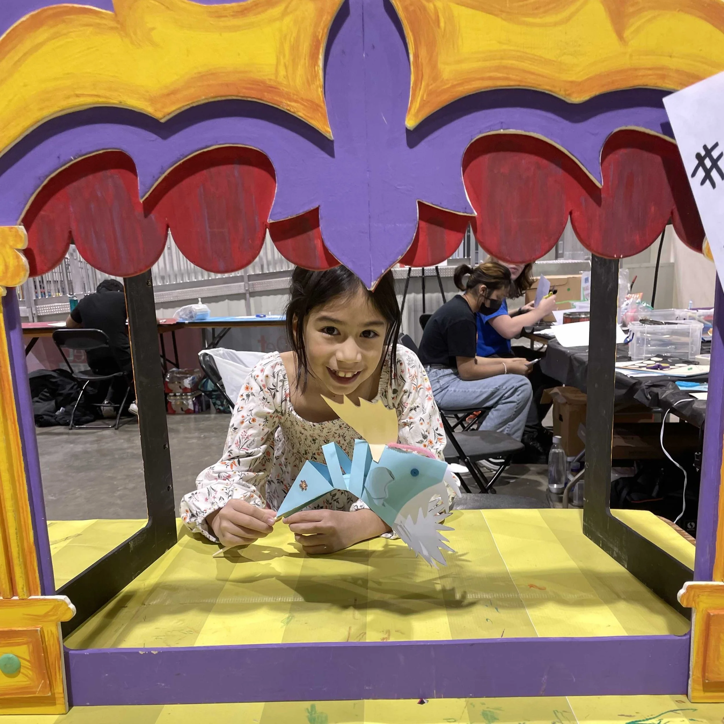 Child shows a paper puppet in a colourful stage