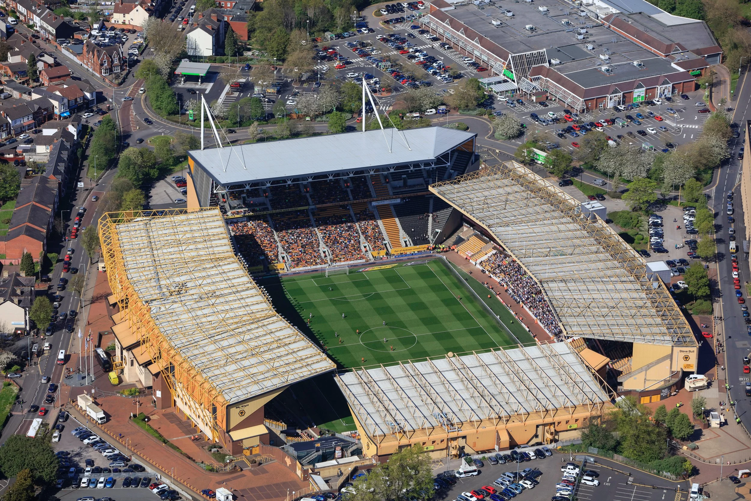 Aerial view of a stadium with fans, surrounded by parking lots and urban buildings.
