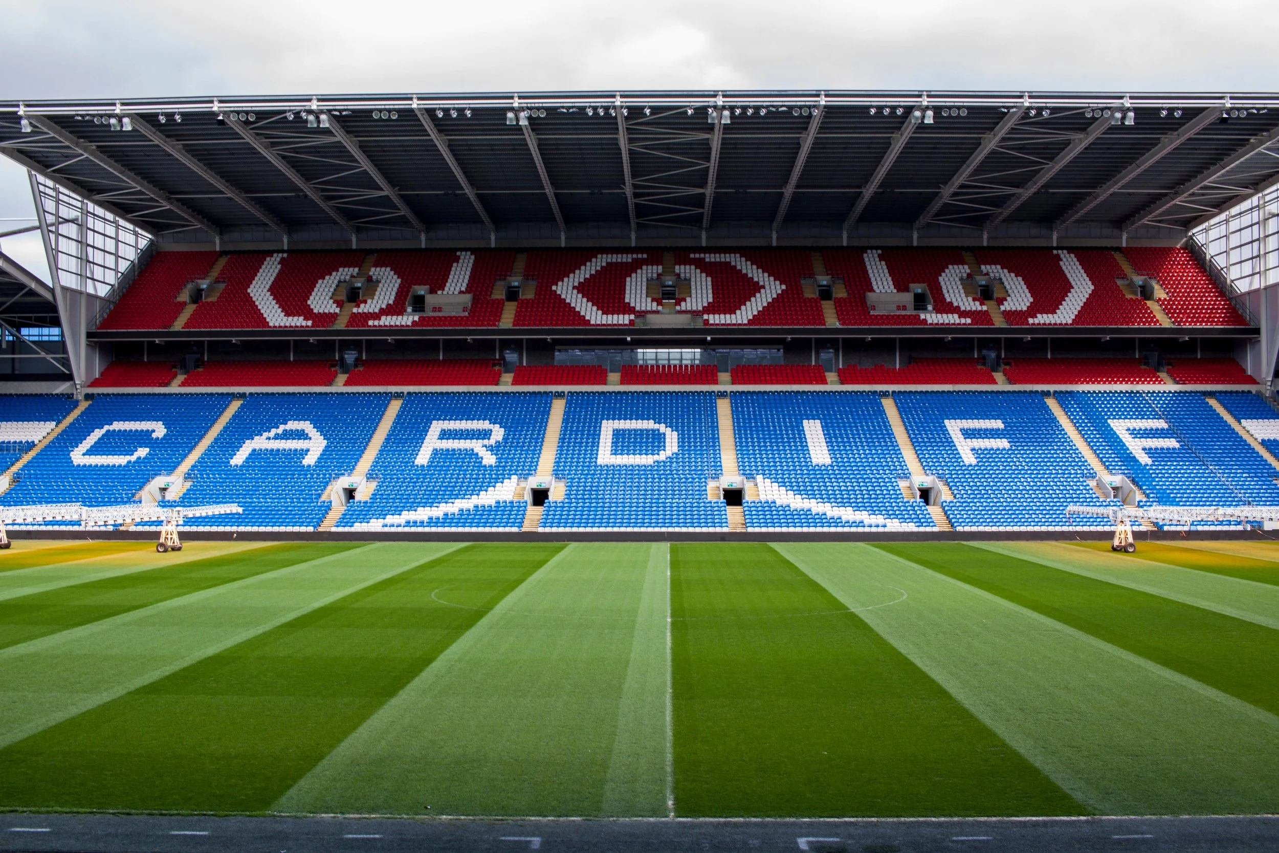 Empty soccer stadium with red and blue seats, displaying the words 'POLAND' and 'CARDIFF' in the stands, and a freshly mowed green field.