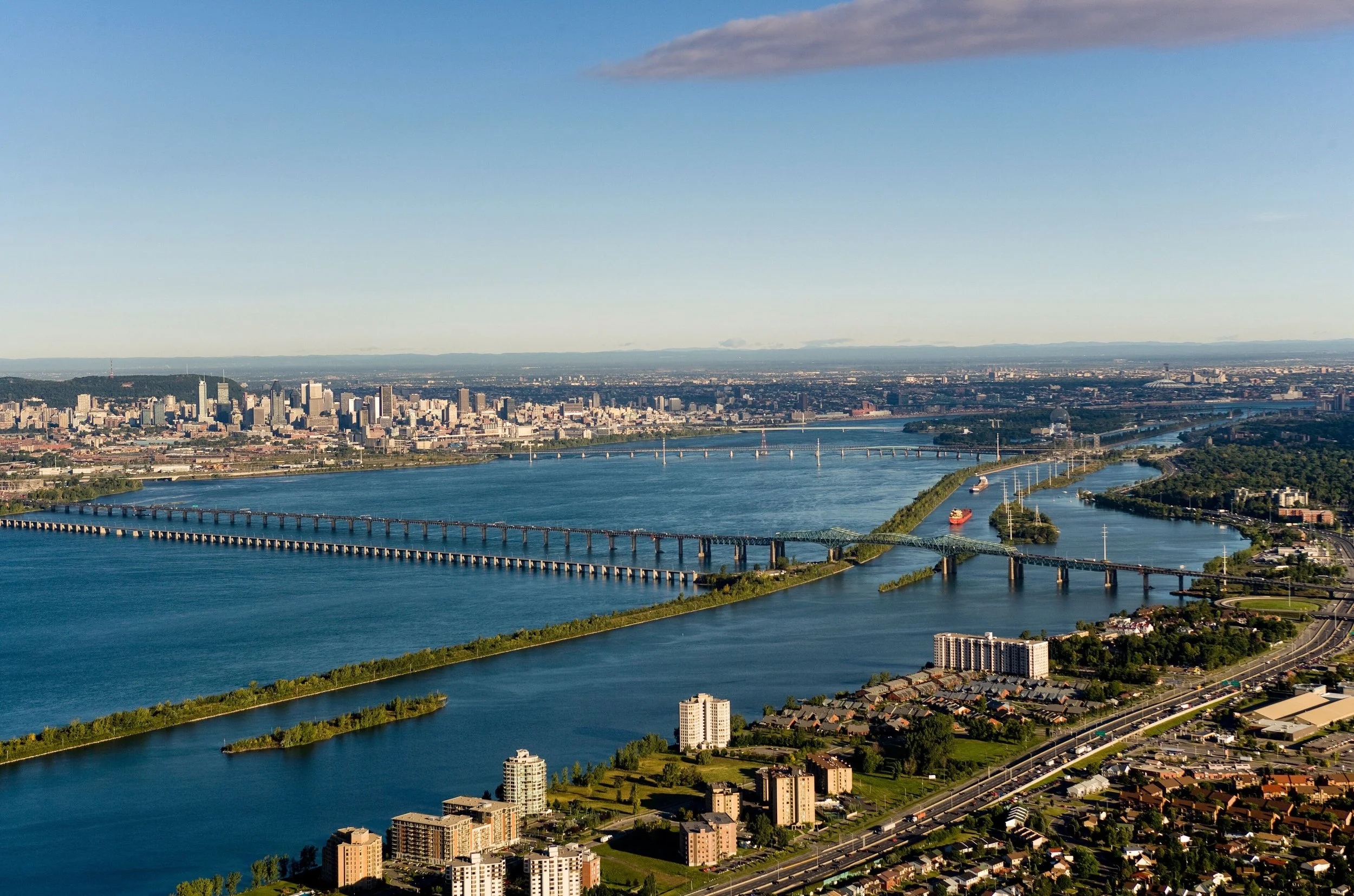 Vue aérienne d'une ville avec un fleuve, plusieurs ponts, des bâtiments modernes et une zone verte dans le contexte d'un ciel clair.