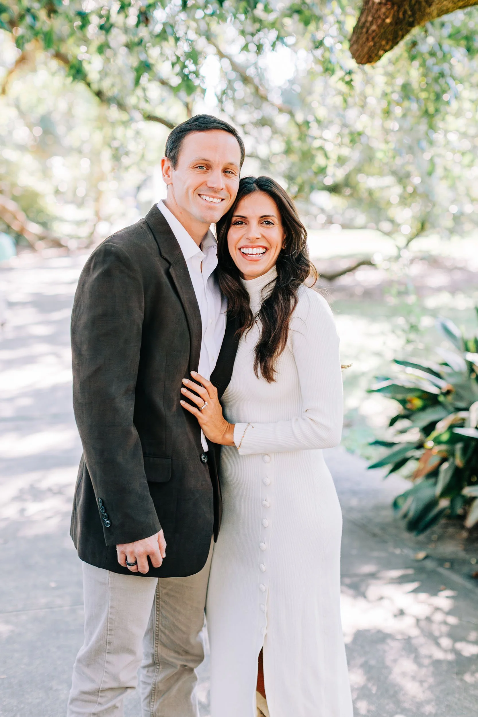 Smiling man and woman standing close together outdoors in a park, with trees and greenery in the background