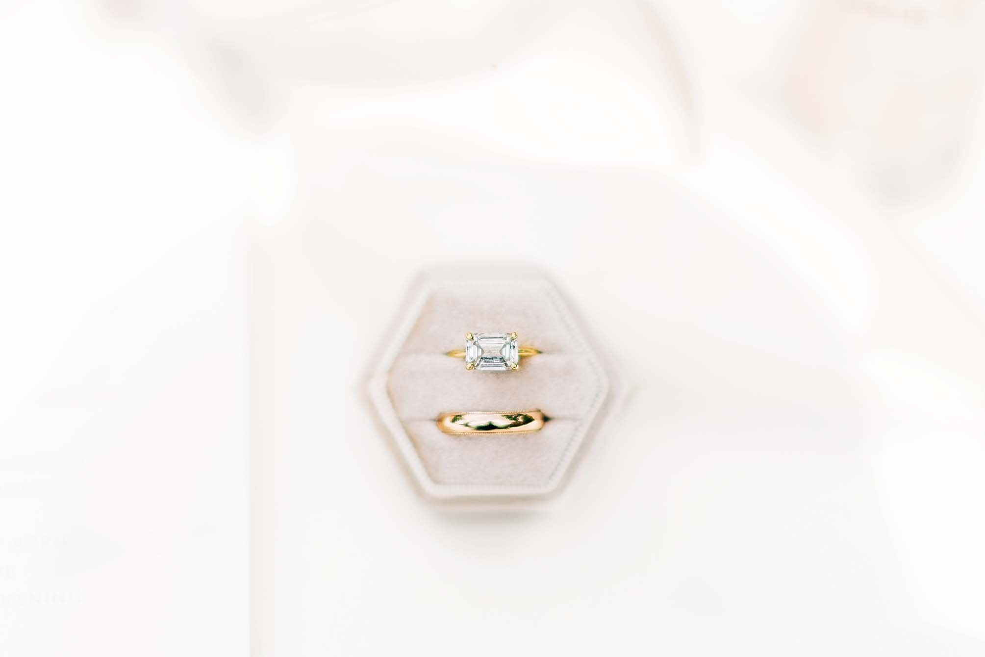 A diamond engagement ring with an emerald cut gemstone in a white and gold setting, displayed in a jewelry box.