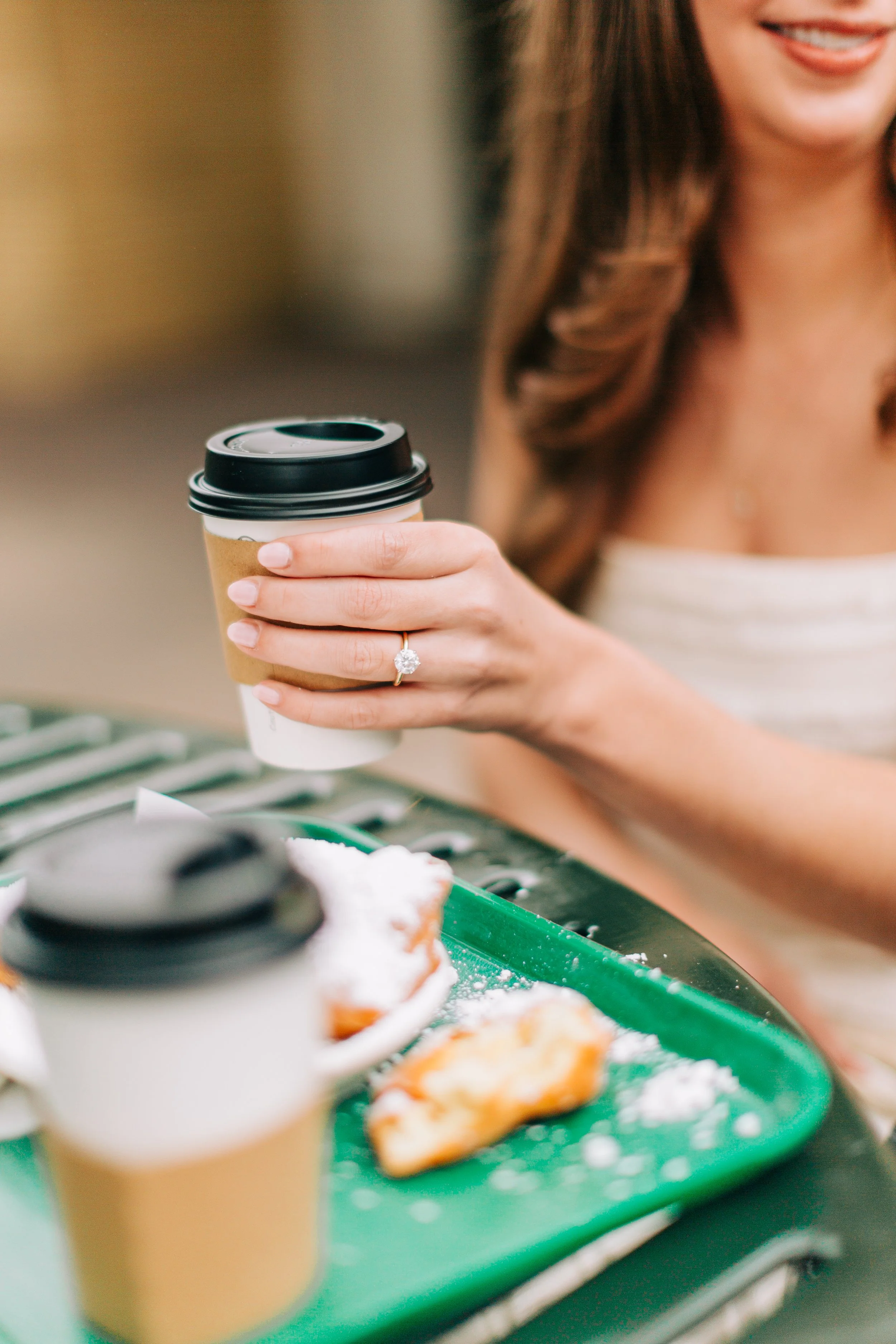 bride holding coffee cup showing engagement ring, couple having coffee at cafe du monde during engagement photography with sarah shaw