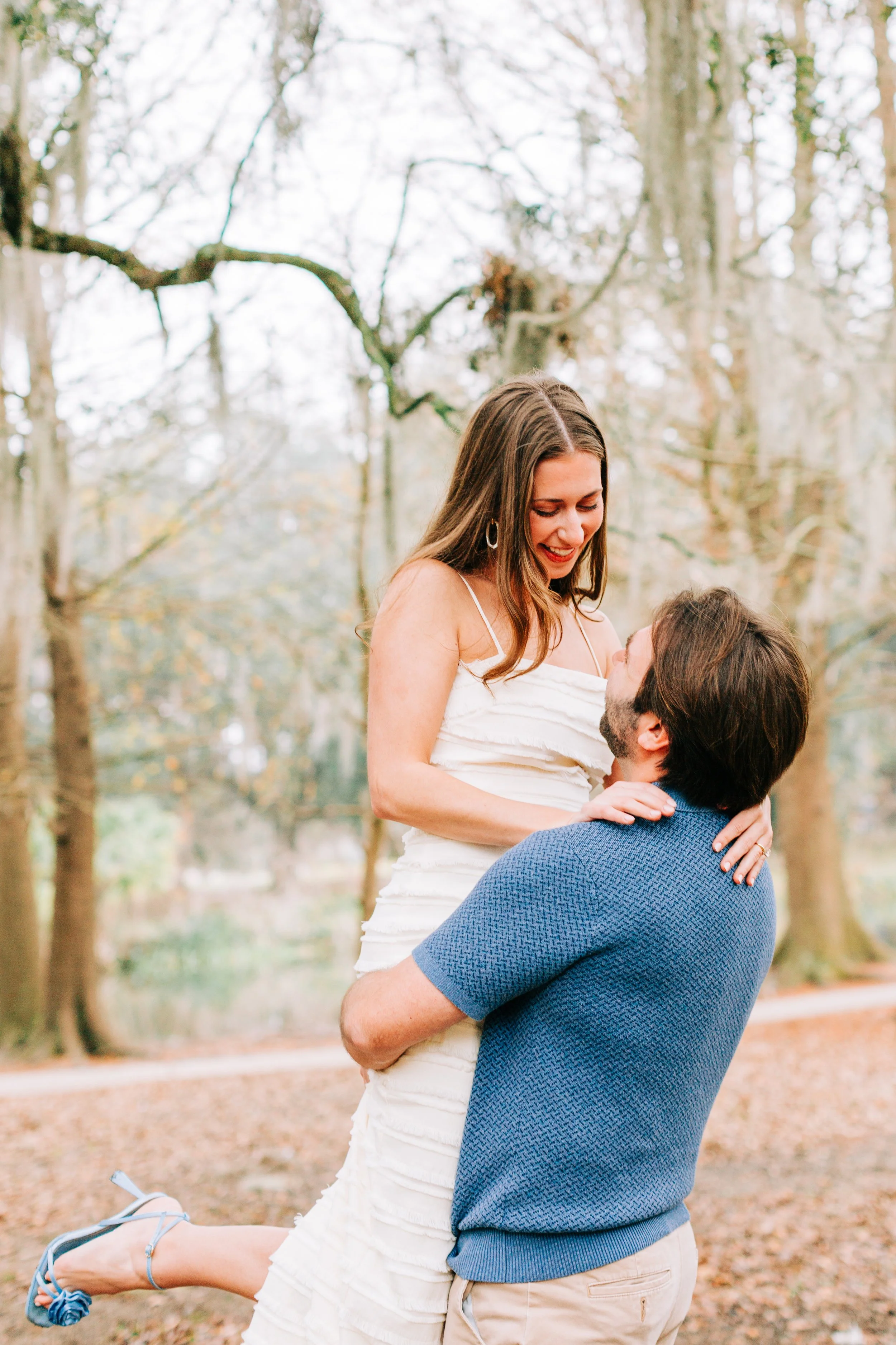 victoria and patrick’s new orleans city park engagement photos, man lifting woman off the ground in city park, woman smiles at man, baton rouge wedding photography