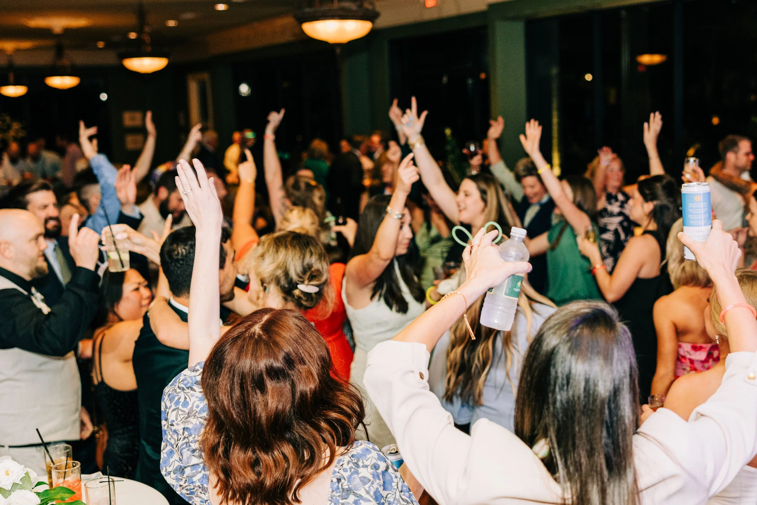 crowd of people dancing with hands in the air at an indoor wedding reception in the neptune at houmas house in baton rouge, baton rouge wedding photography