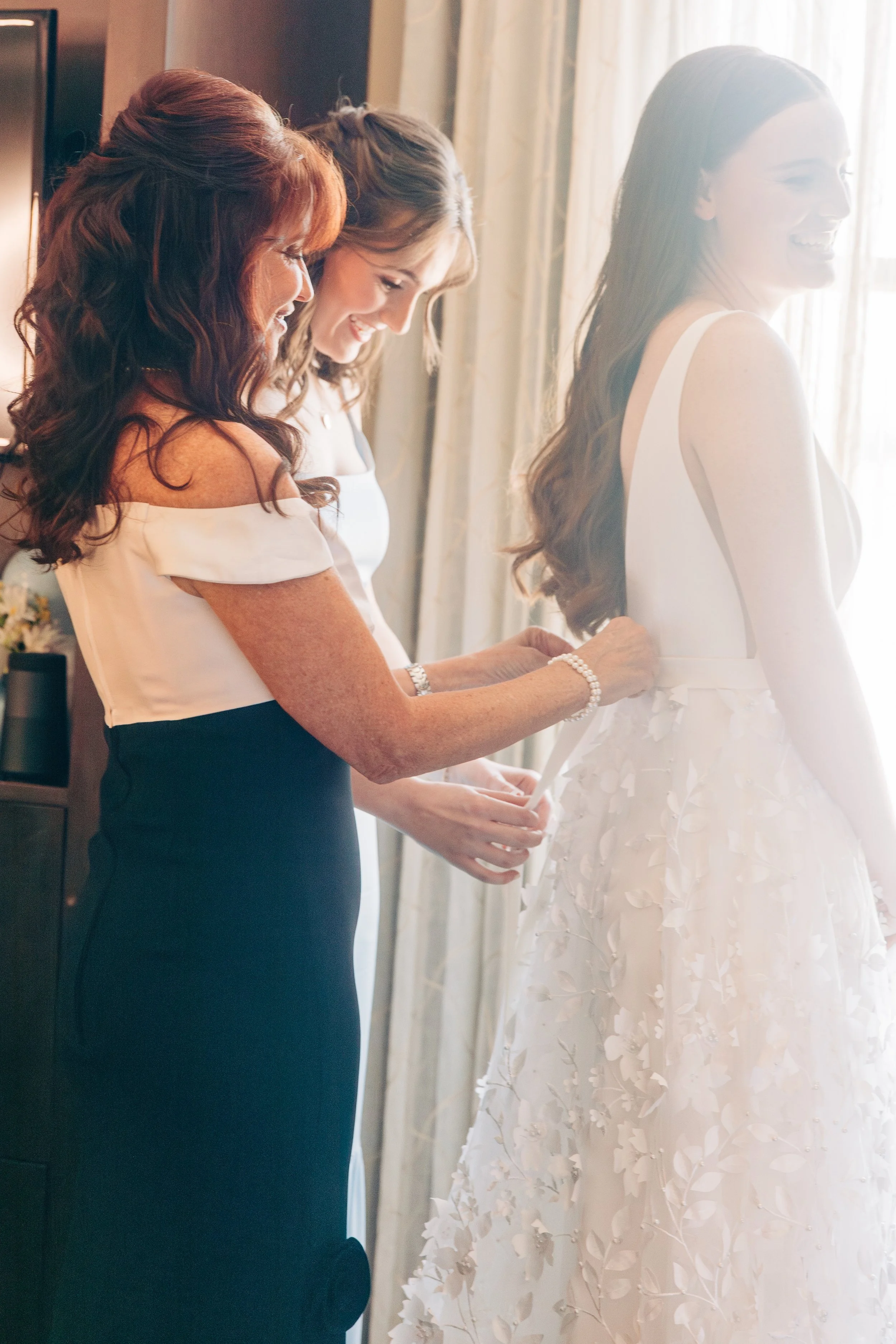  Bride putting on wedding dress with her mother and maid of honor in bridal suite at Baton Rouge wedding at St. Aloysius Catholic Church and Louisiana Old State Capitol 