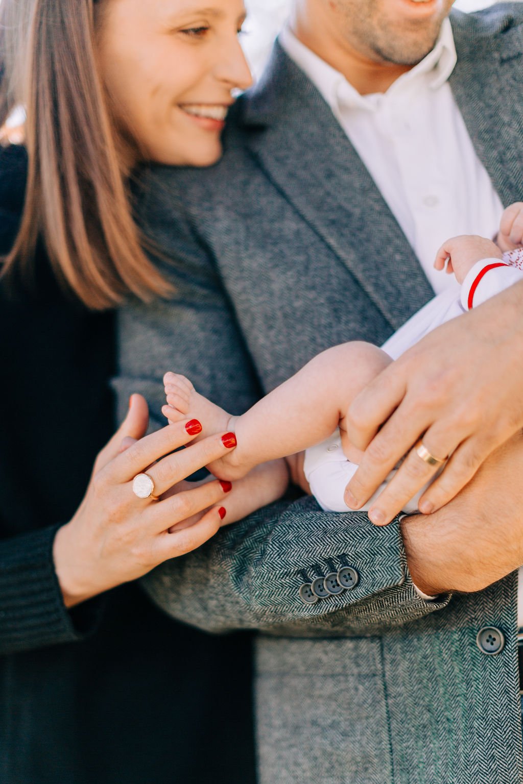 close-up of mom and dad’s hands over baby’s body while standing, holding and looking down at newborn baby during family portrait session in baton rouge