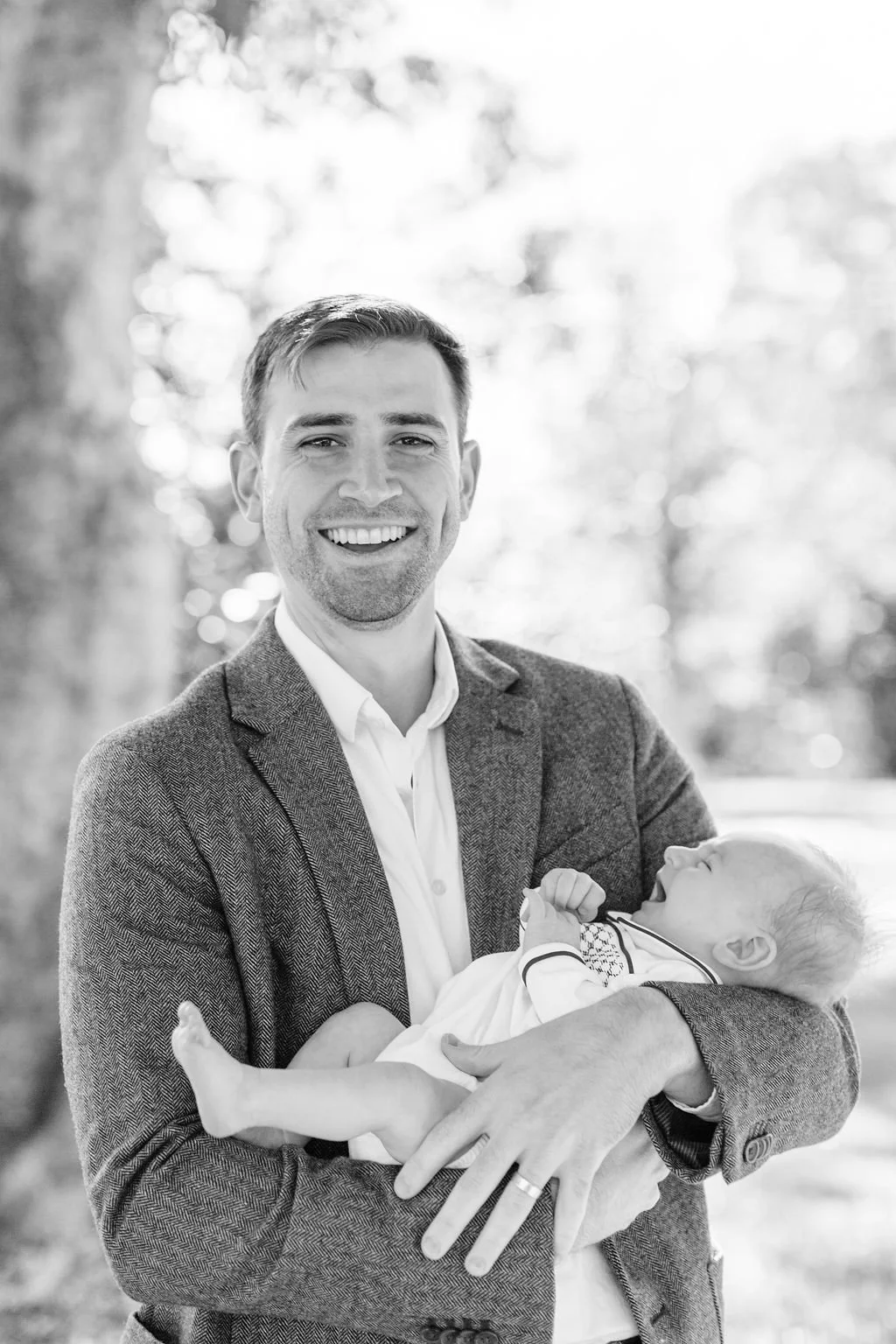 black and white moment of dad standing and holding newborn baby during family portrait session in baton rouge