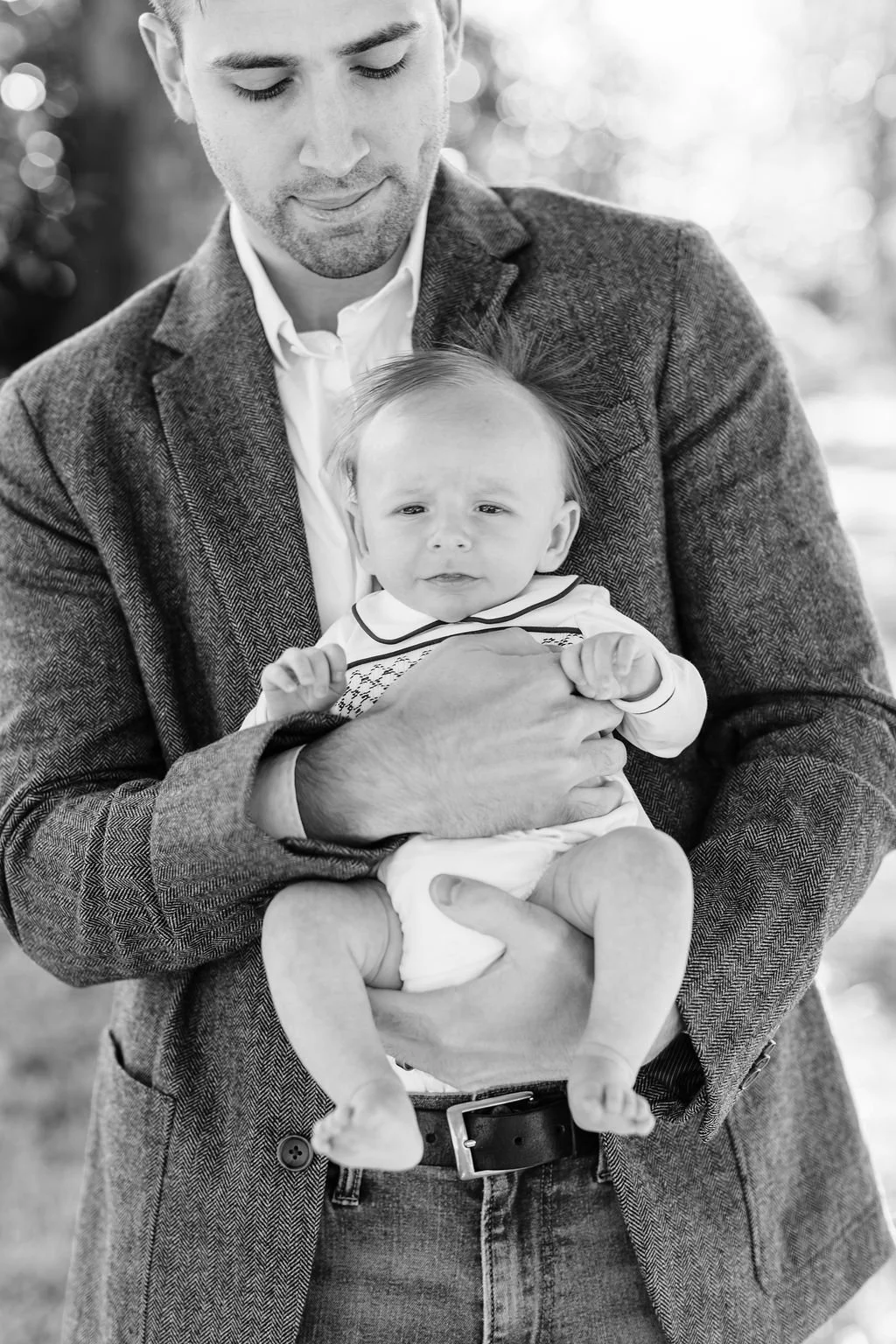 black and white moment of dad standing and holding newborn baby during family portrait session in baton rouge