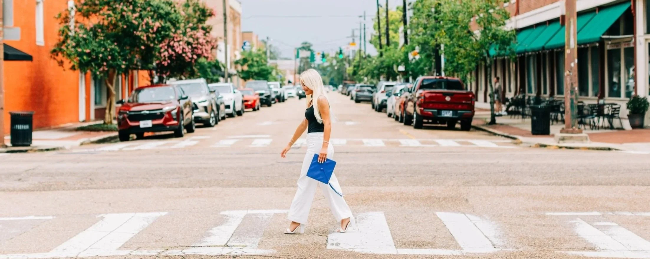 High school senior walking across downtown street holding graduation cap in Baton Rouge
