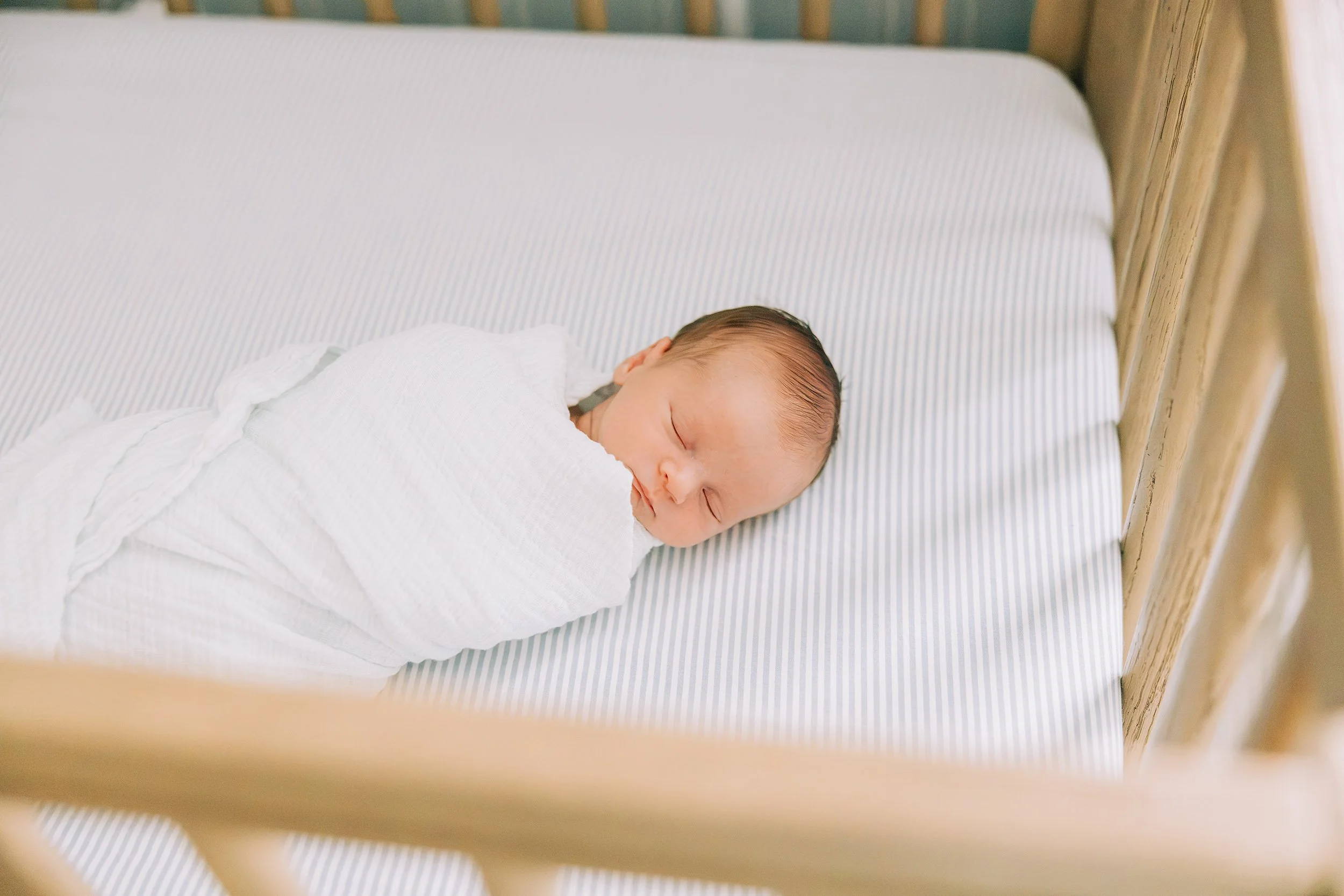 Newborn baby sleeping in a crib with a white blanket.