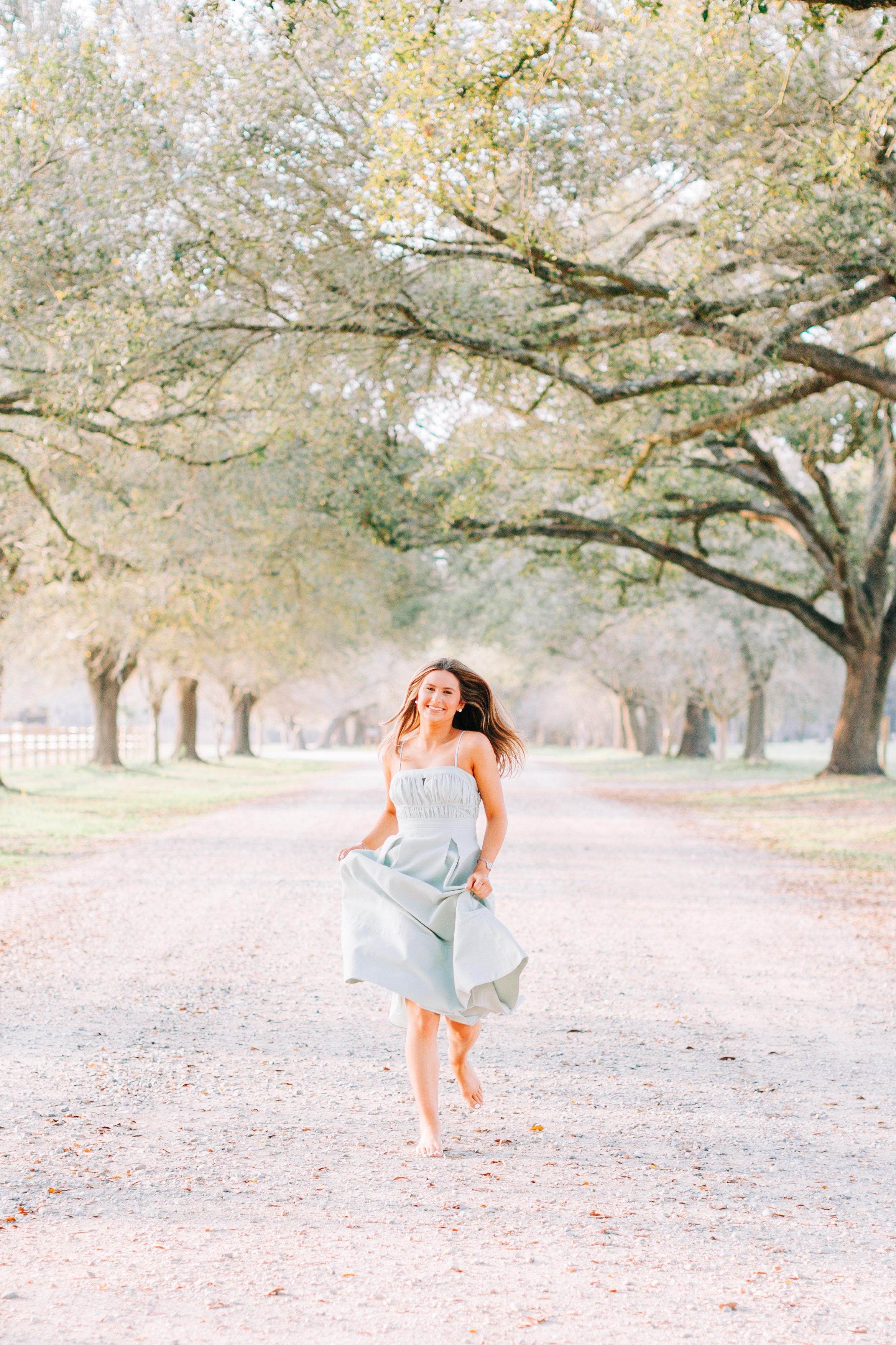 baton rouge senior portraits at burden gardens, brown haired girl running on gravel road in green dress smiling under the trees