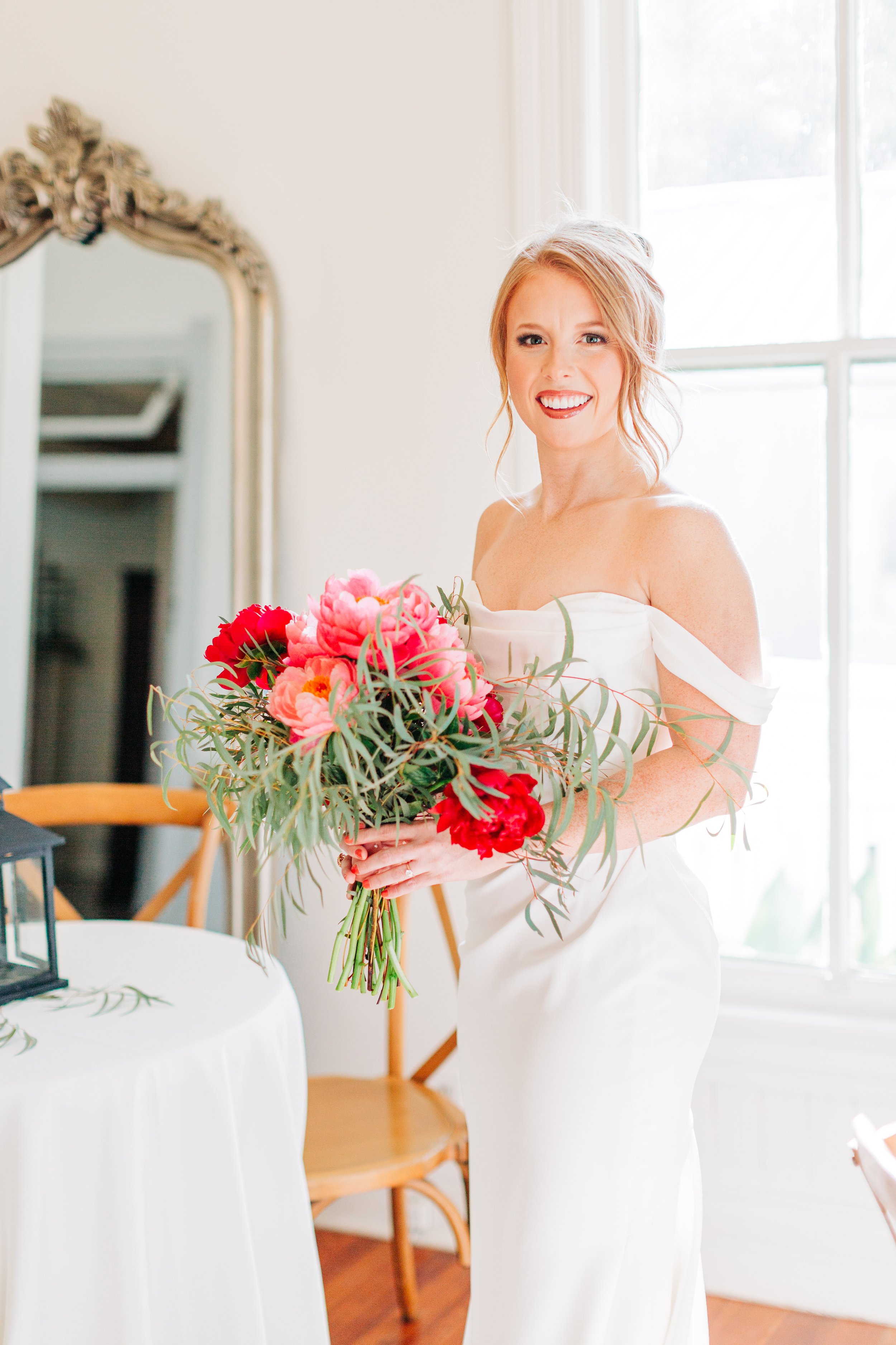 A smiling woman in a white dress holding a bouquet of pink and red flowers.