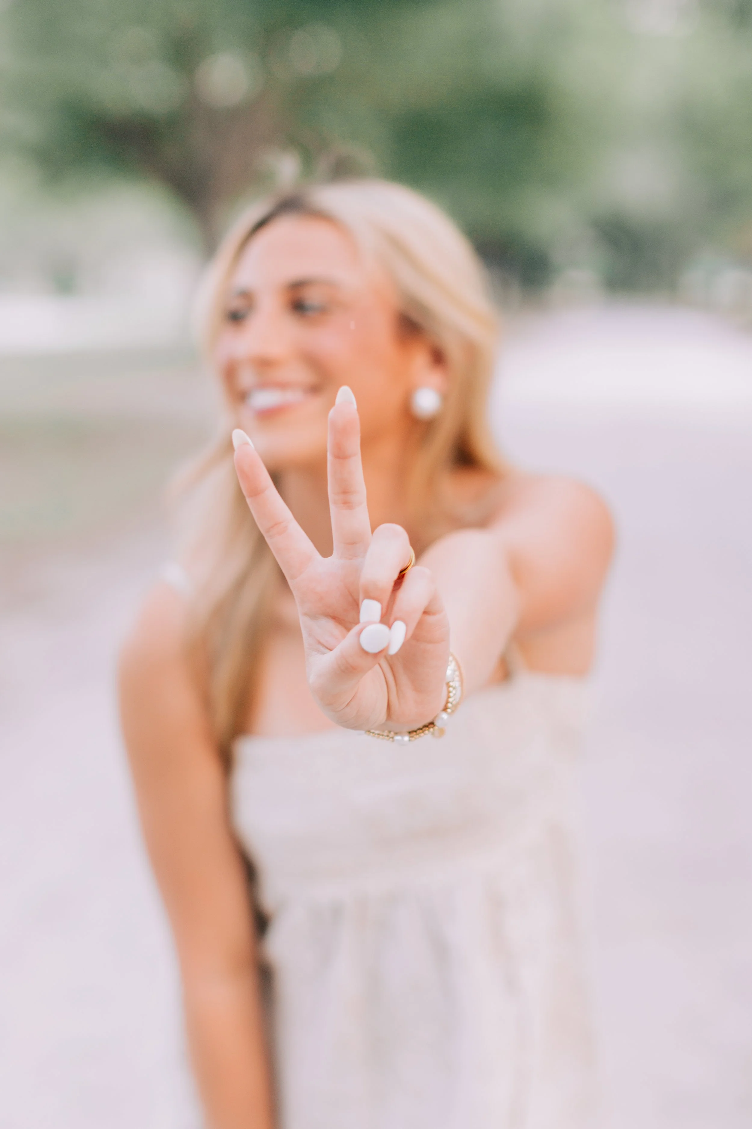 baton rouge senior portraits at burden gardens, blond haired girl making peace sign with her hand, her smiling face is in the background