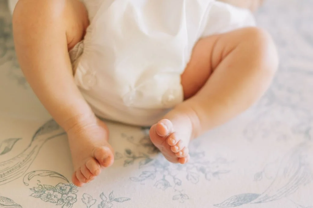 Close-up of a baby’s legs and feet, lying on a patterned surface, wearing a white diaper.