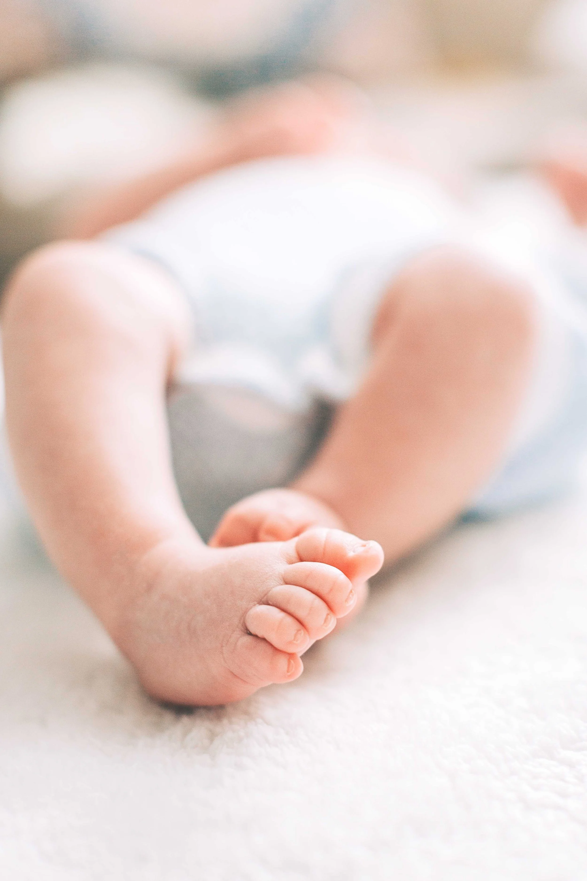 Close-up of a baby lying on a soft surface, holding a small object with its hands.