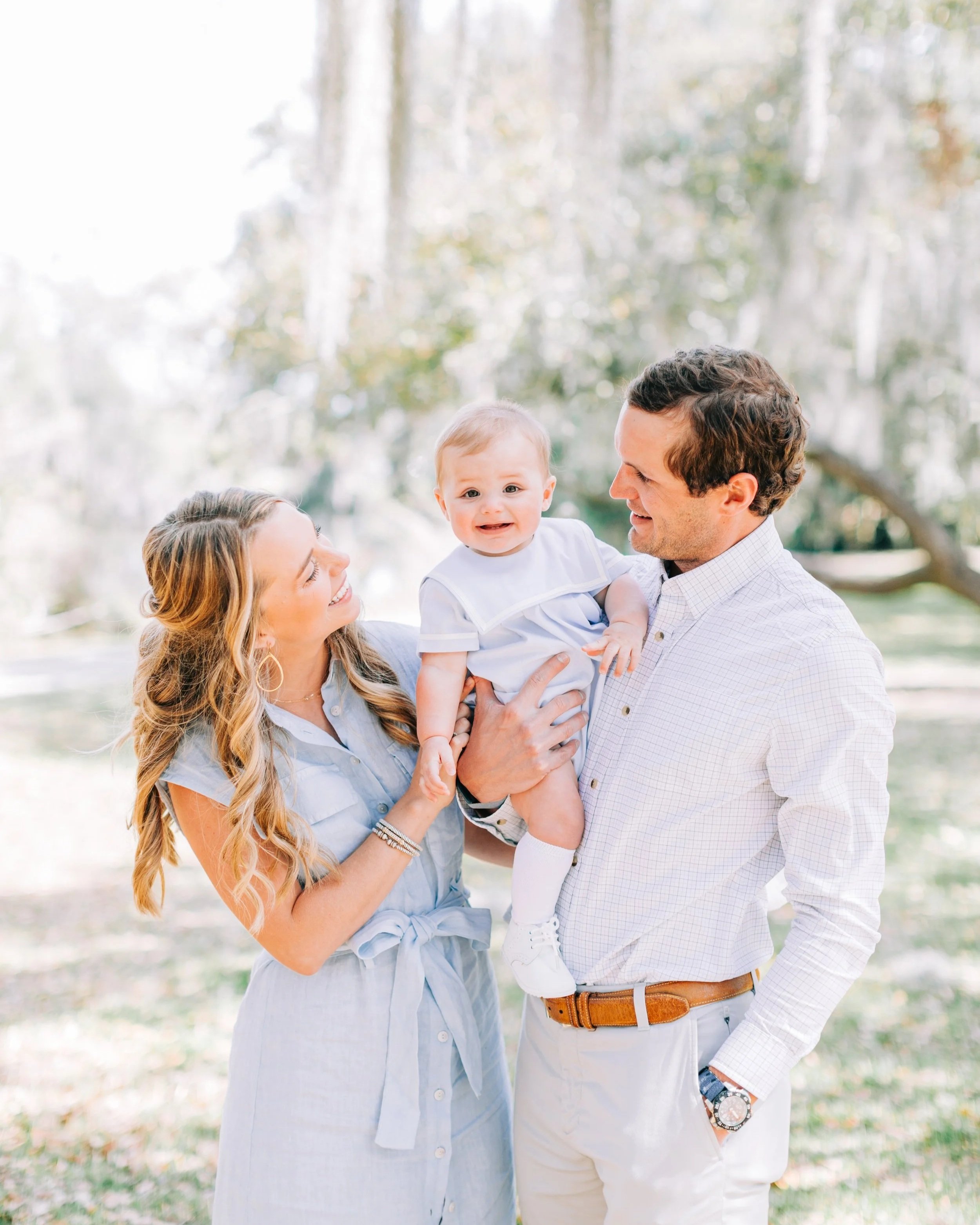 Parents holding their baby and smiling at each other during outdoor family session in Baton Rouge