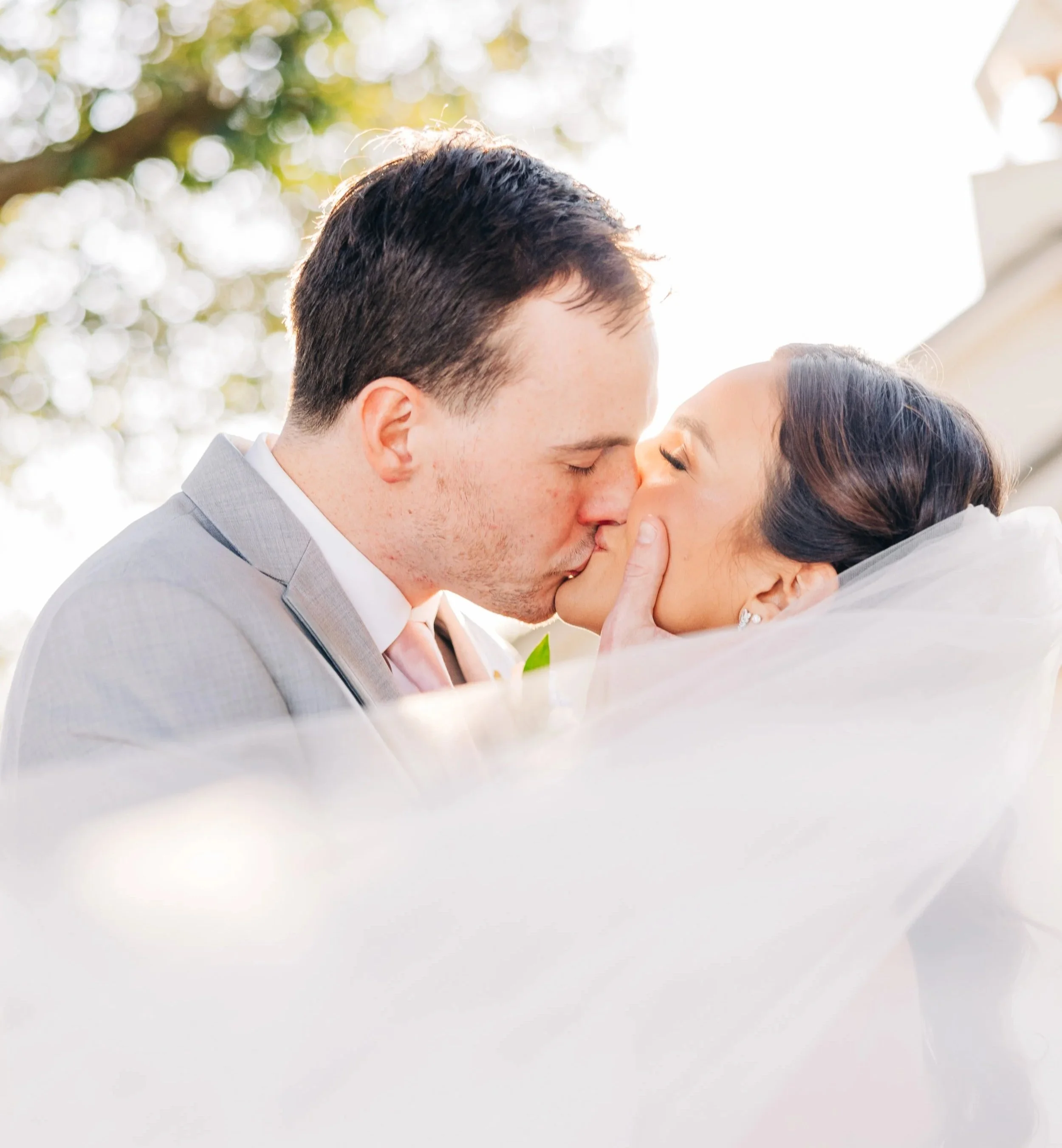 Close-up of bride and groom kissing with soft veil and golden light at a Baton Rouge wedding