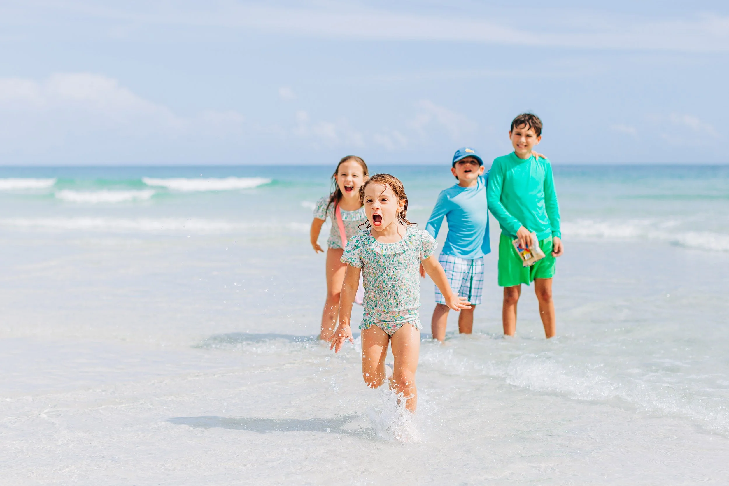 Group of children running and playing in the ocean waves at the beach on a sunny day.