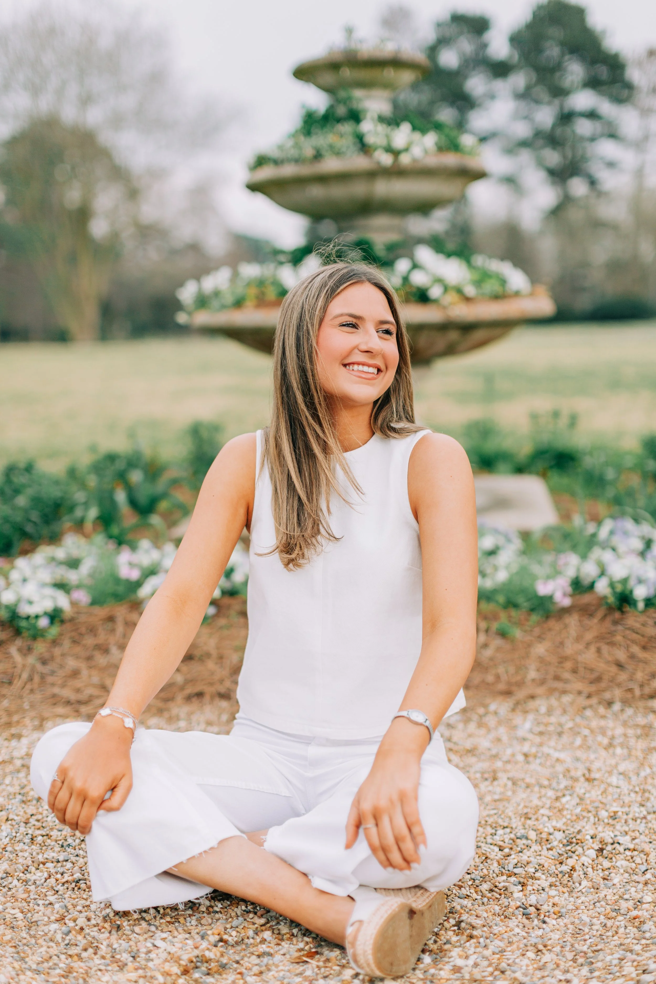 baton rouge senior portraits at burden gardens, brown haired girl sitting indian syle in front of fountain holding flowers