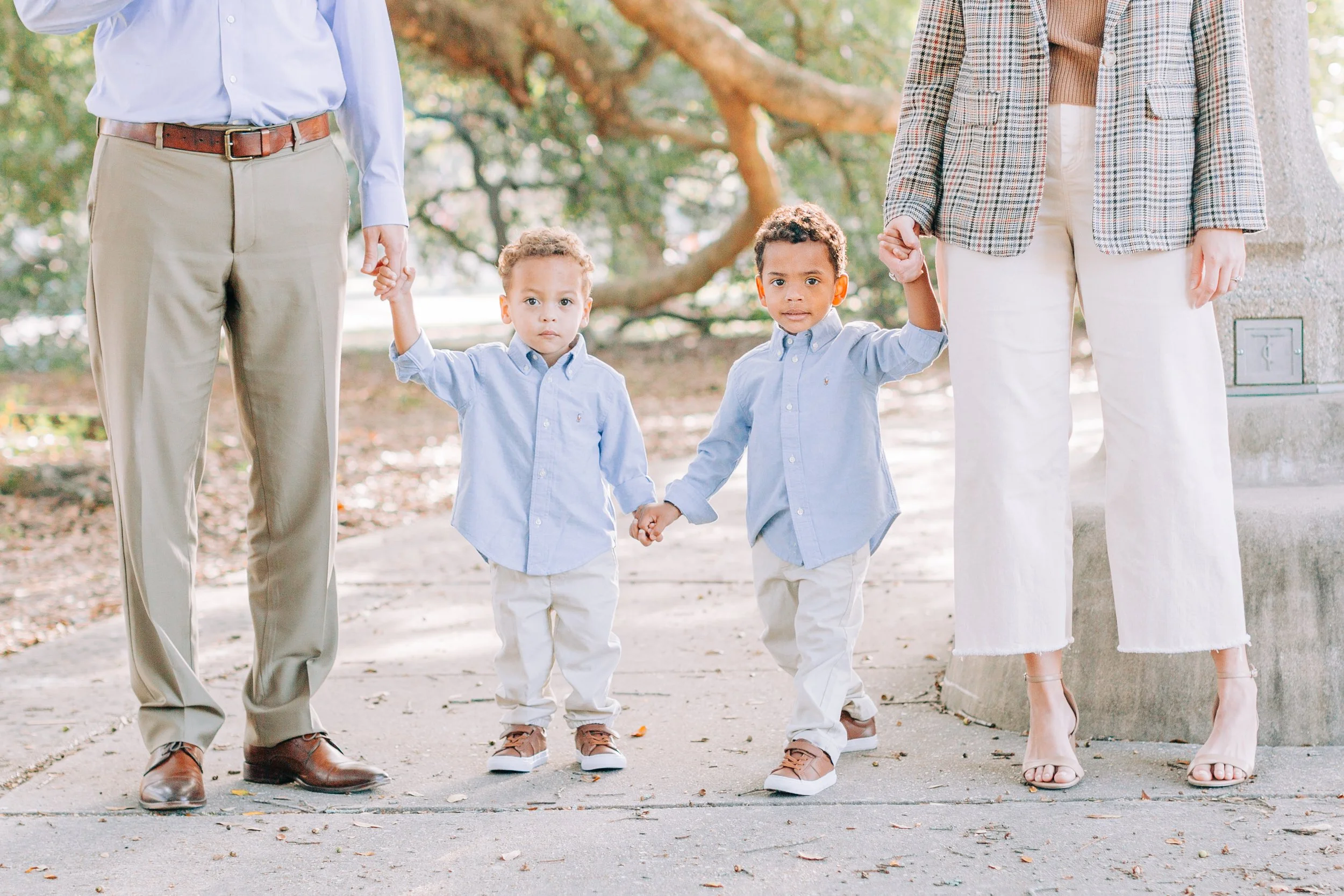 Two young boys holding hands between an adult man and woman in a park with trees in the background.