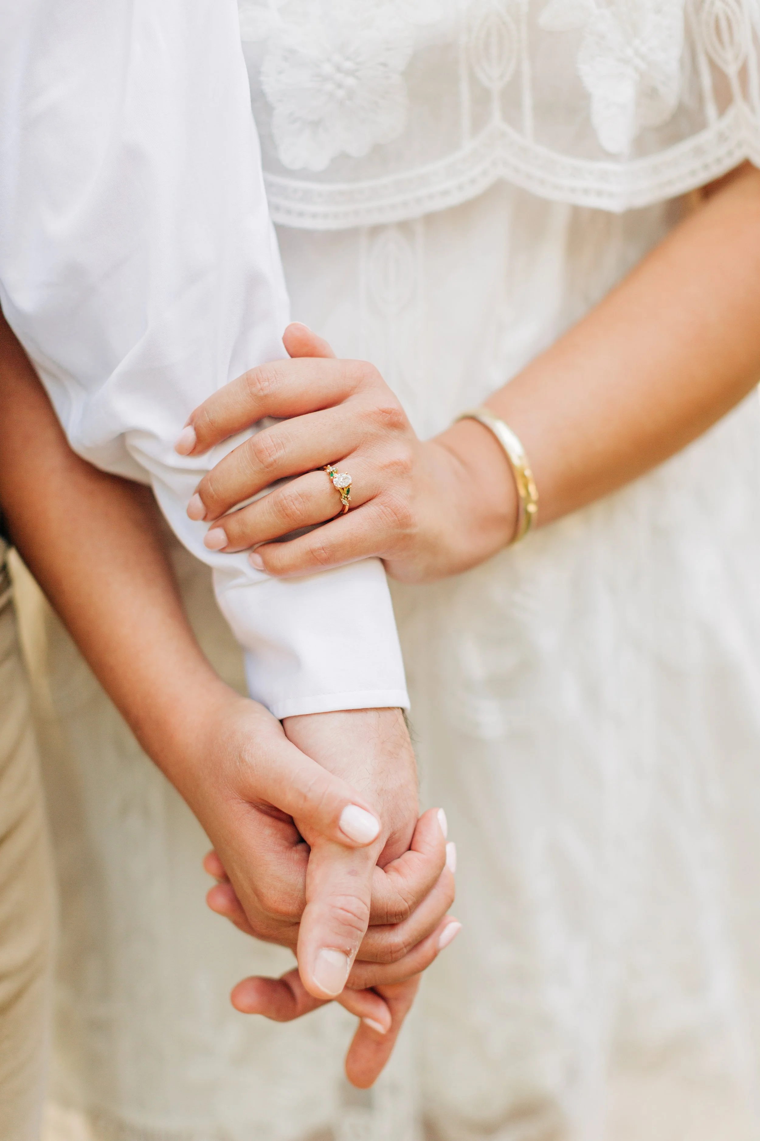 Close-up of a person wearing a gold ring with a large clear gemstone, holding hands with another person.