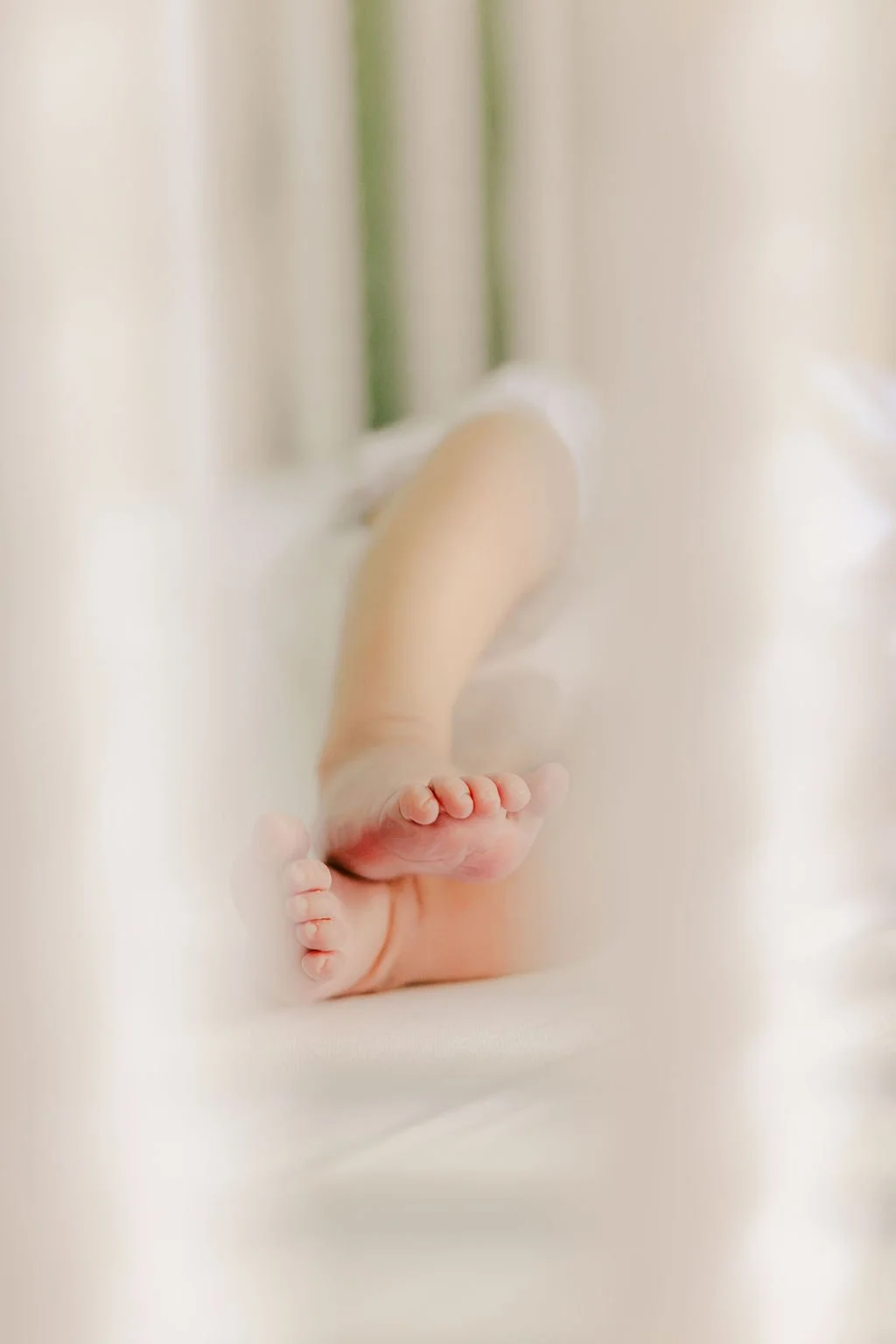 Close-up of a baby's feet and legs as the baby lies on their stomach in a soft, light-colored setting.