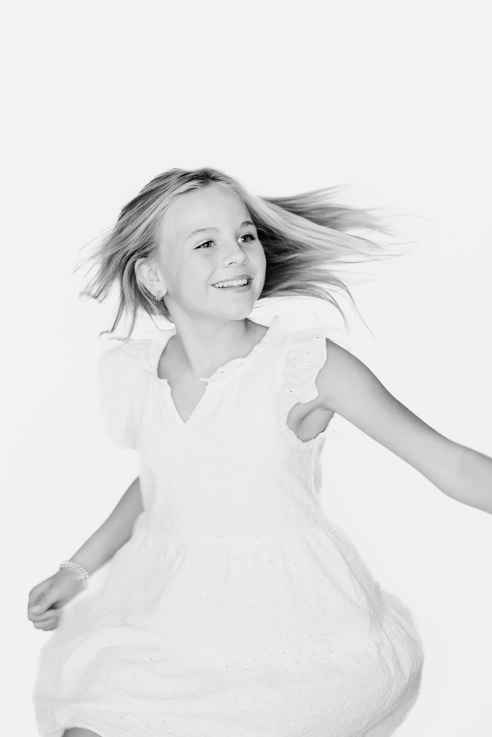 A young girl in a white dress smiling and looking to her left, with her hair flowing.