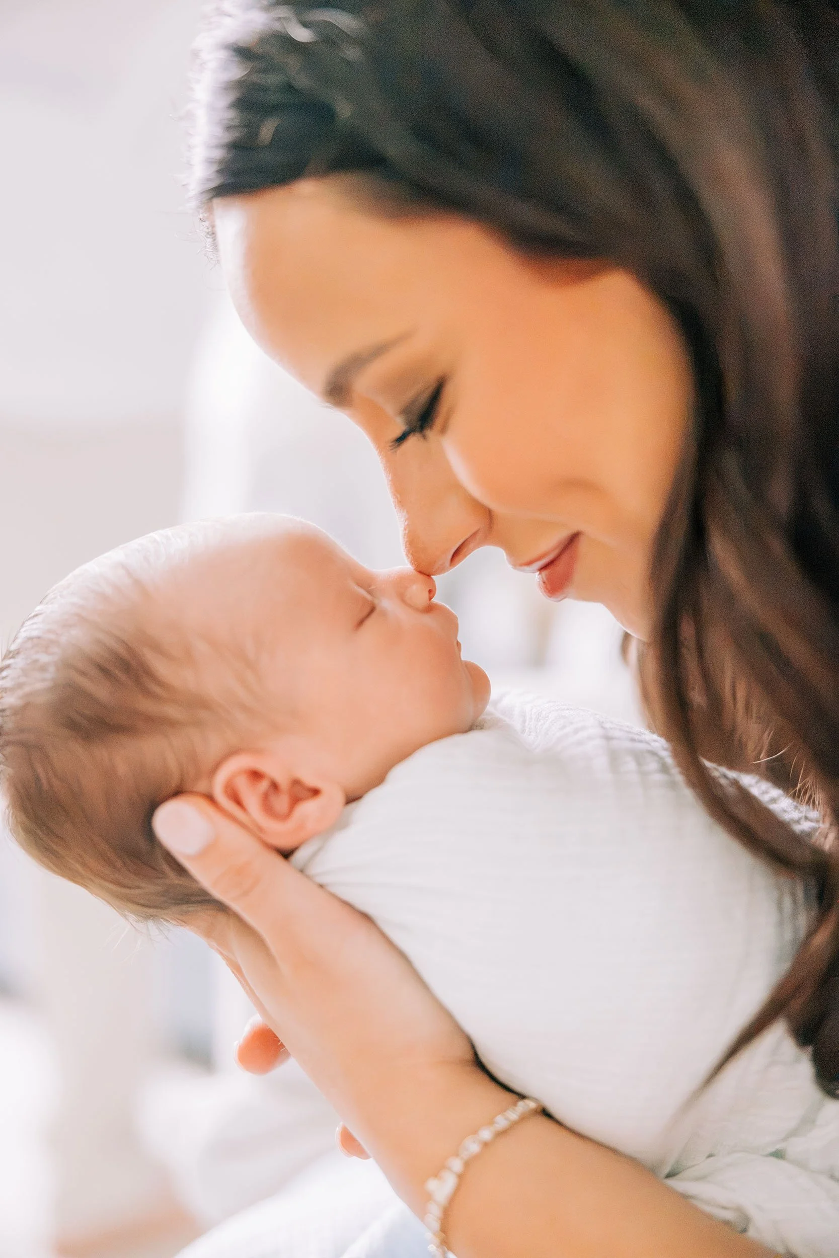A woman holding a baby close to her face, gently touching noses with a loving expression.