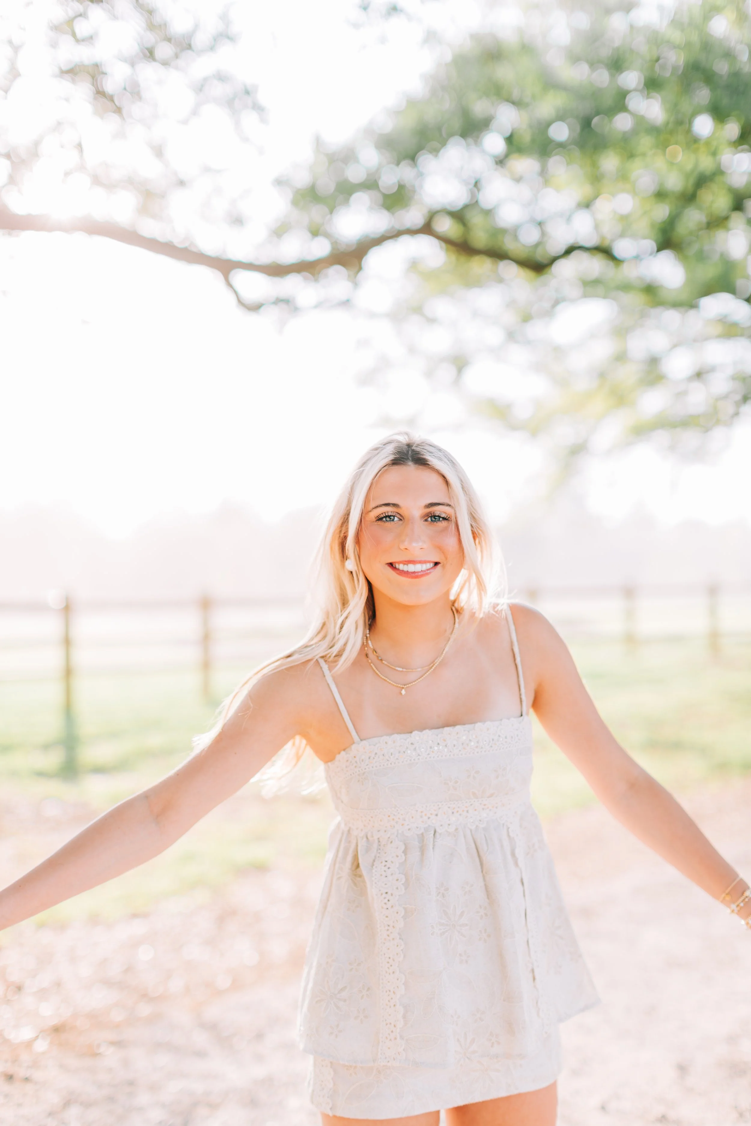 baton rouge senior portraits at burden gardens, blond haired girl spinning around, arms out, smiling under the tree