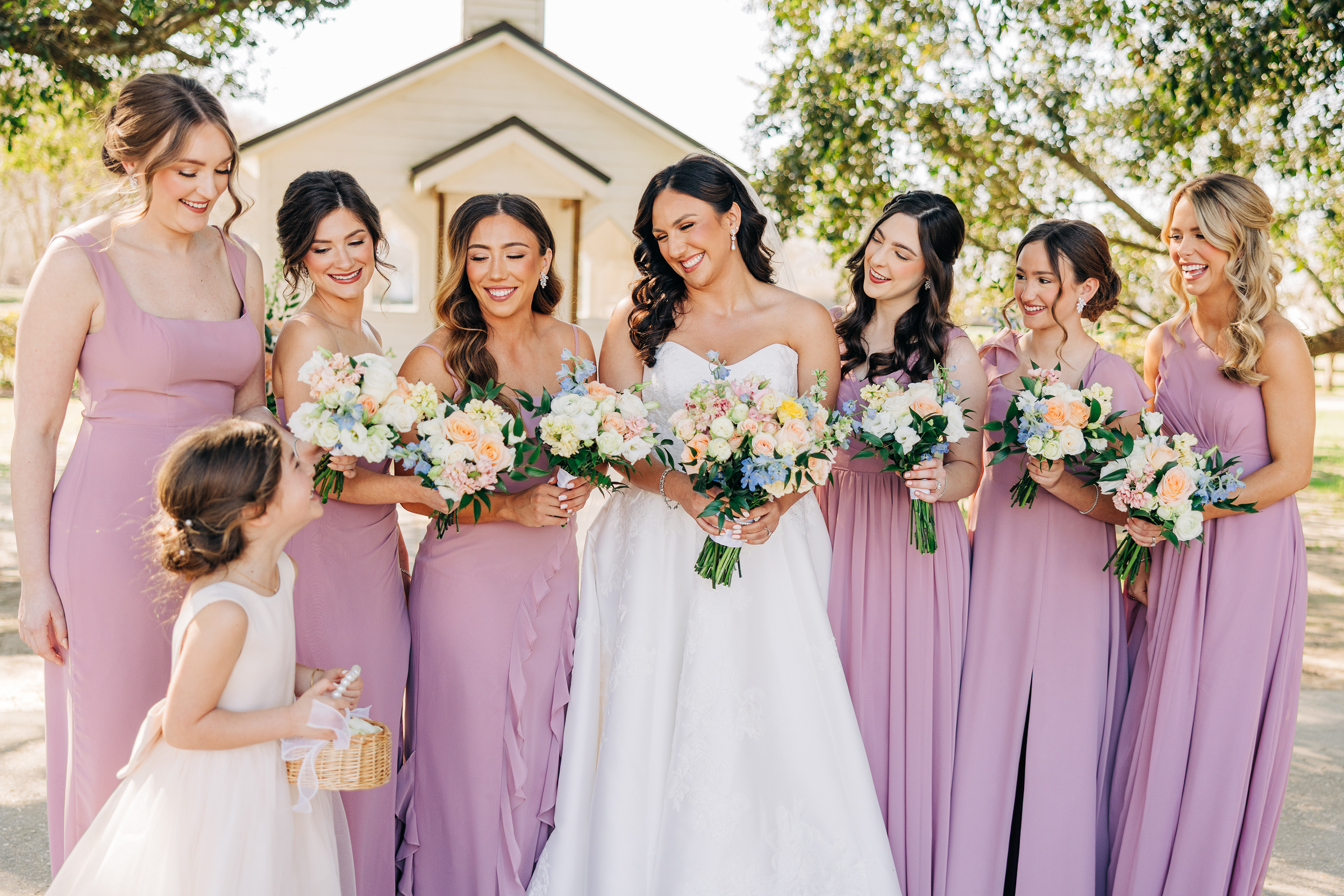 bride and bridesmaids standing in a line smiling down at the flower girl, bridesmaids wearing mauve pink dresses