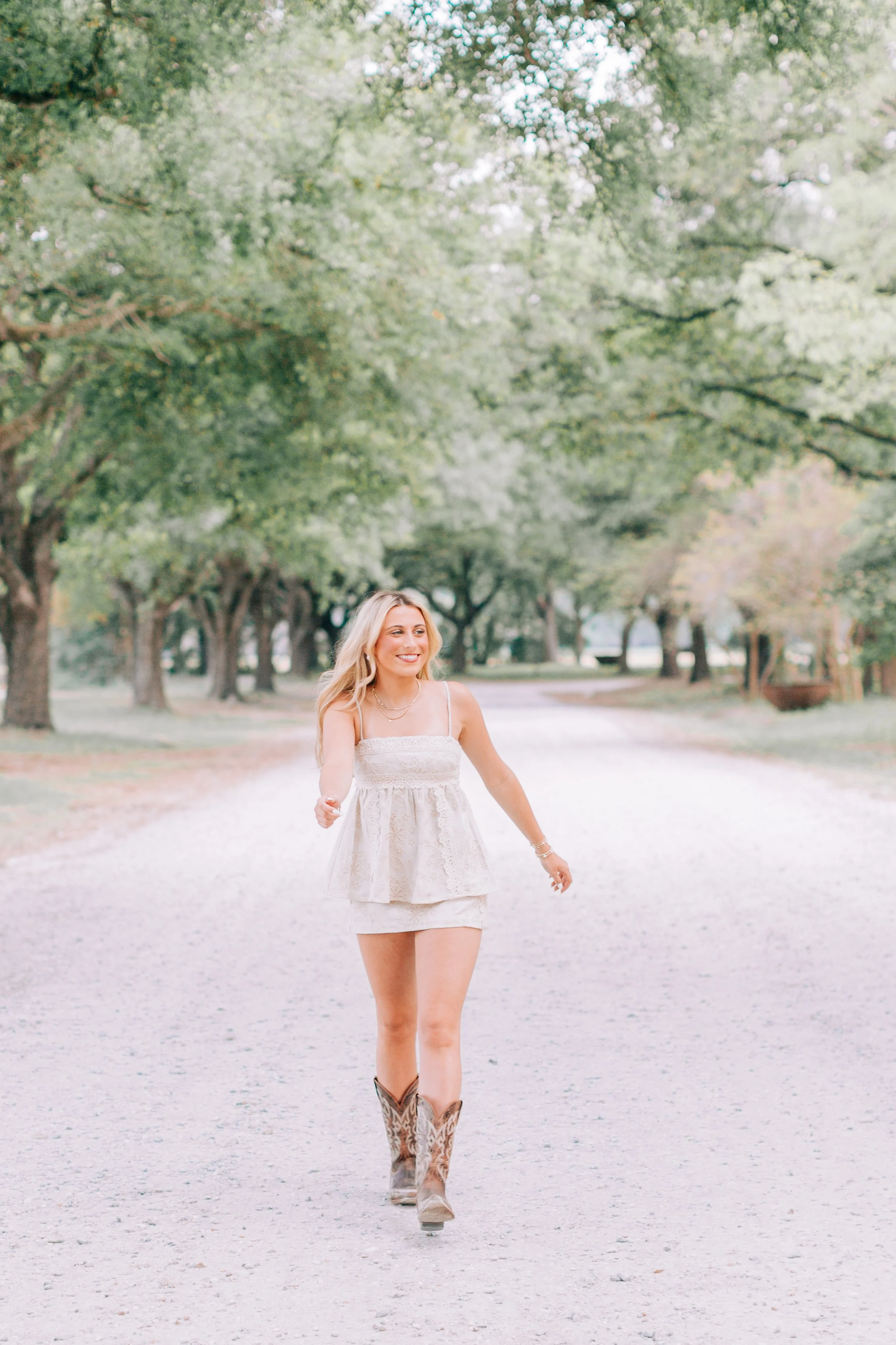 baton rouge senior portraits at burden gardens, blond haired girl walking on tree-lined gravel road 