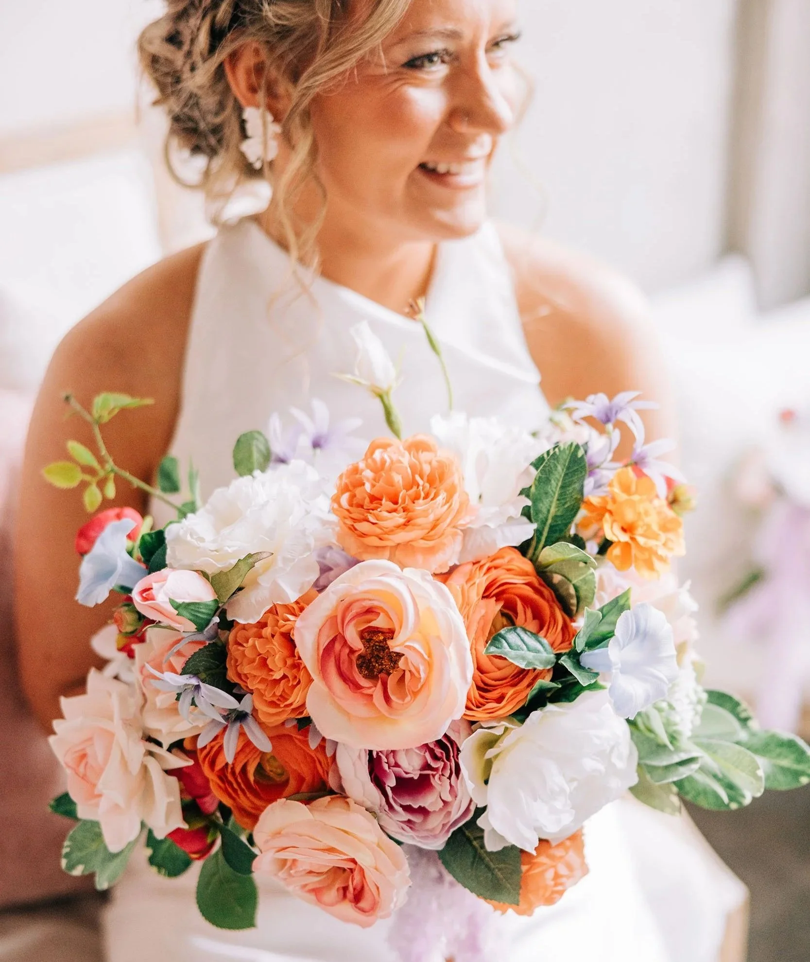 Close-up of a smiling woman with curly hair holding a bouquet of orange, white, and purple flowers.