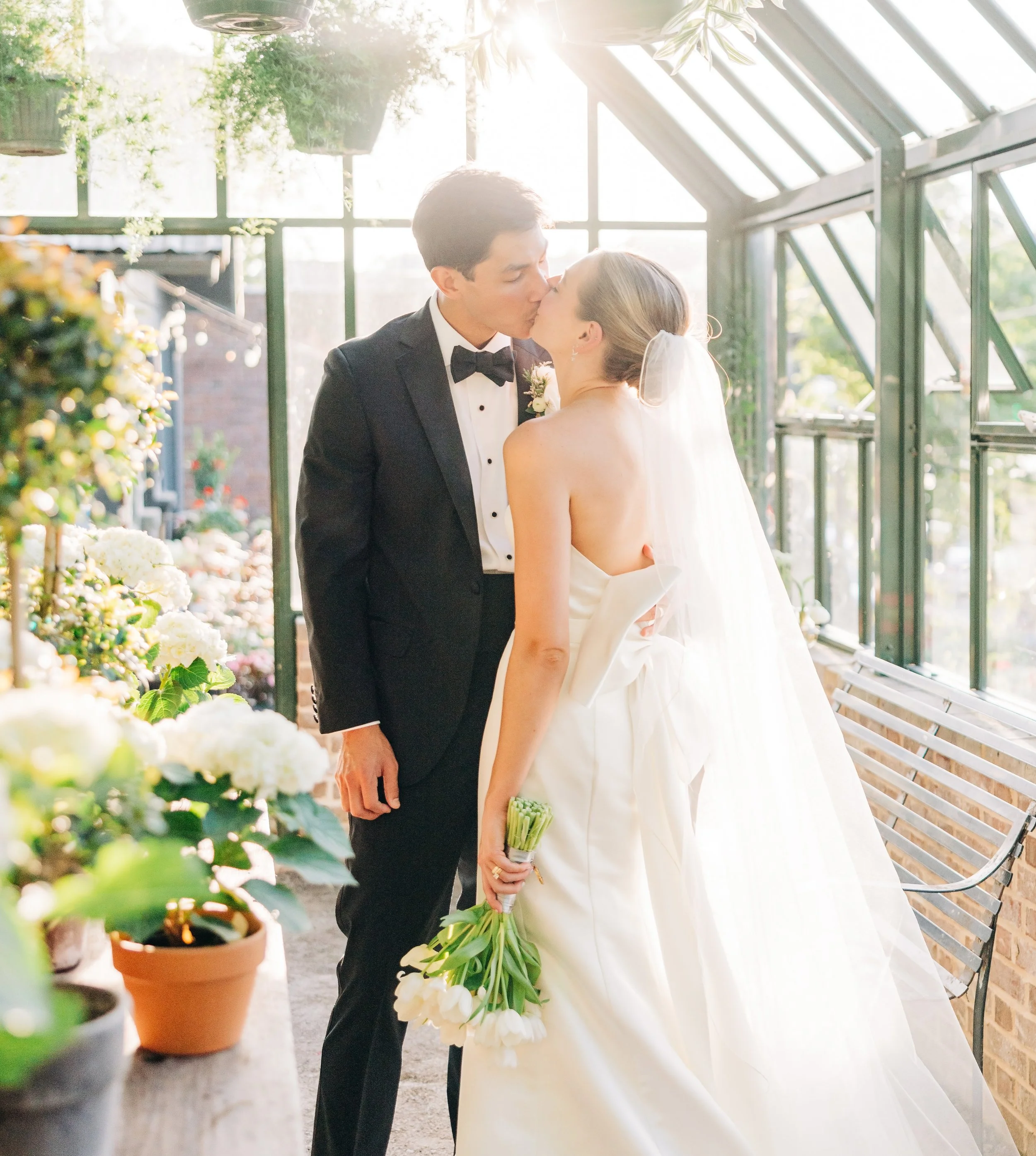 Bride and groom kissing inside a greenhouse with soft light and greenery during a Baton Rouge wedding