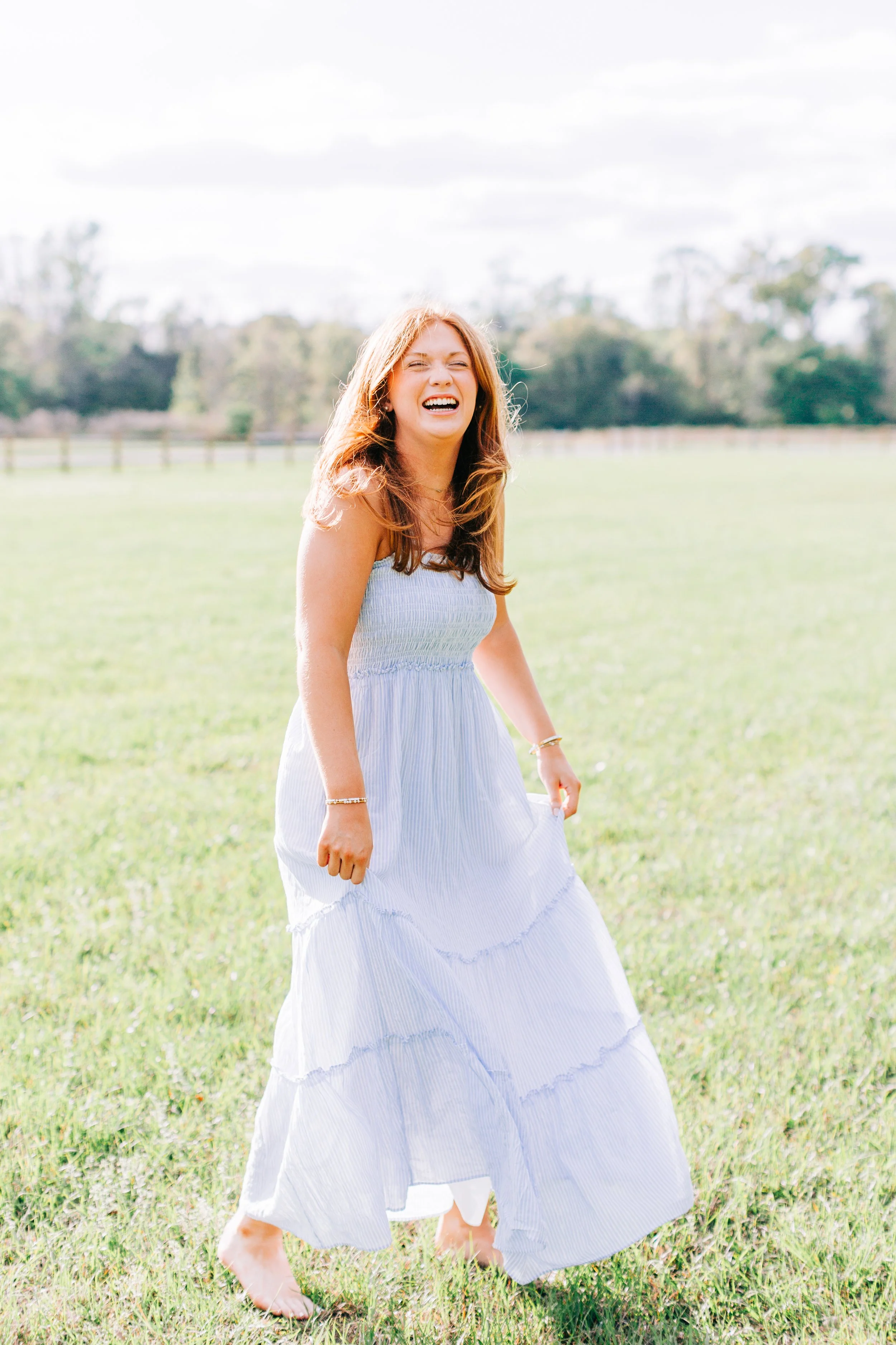 red headed senior portrait in blue dress laughing in a green field at burden gardens in baton rouge