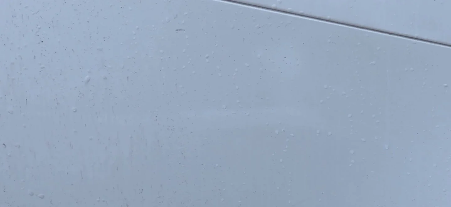 Close-up of a rain-dappled light blue surface, possibly a car door or panel, with a faint horizontal line indicating separation between two sections.