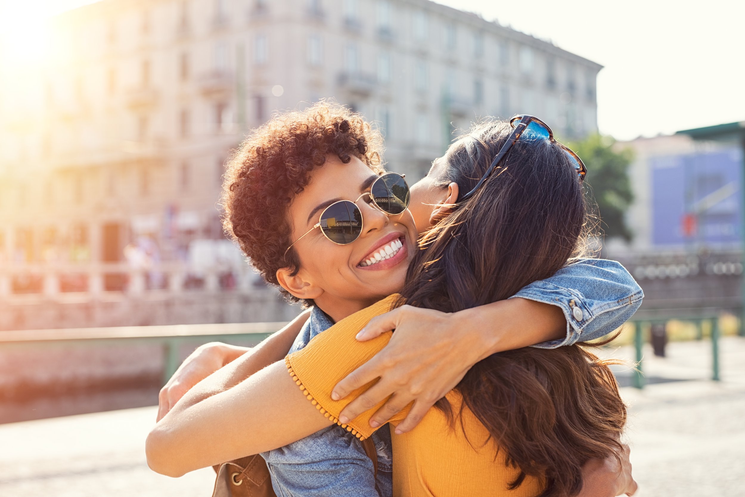 Deux jeunes femmes, dans un environnement urbain, s'étreignent chaleureusement.