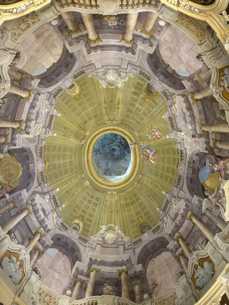 Baroque-style church ceiling with ornate gold and white decorations, painted angels, and a central oval painting of a biblical scene.