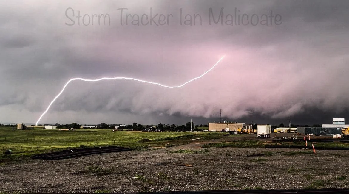 Lightning bolt striking near rural buildings during a storm, with a cloudy sky in the background.